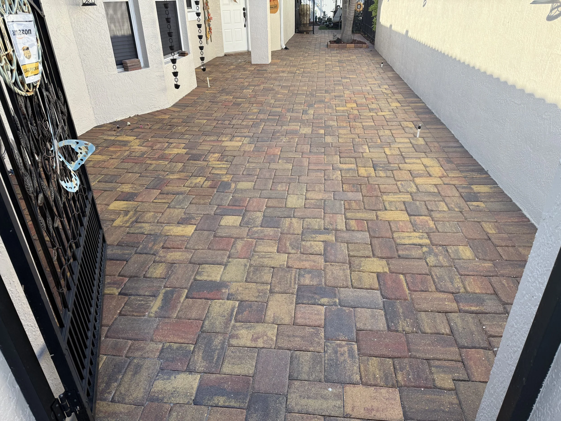 Brick-paved walkway between white building walls, leading past a black gate.
