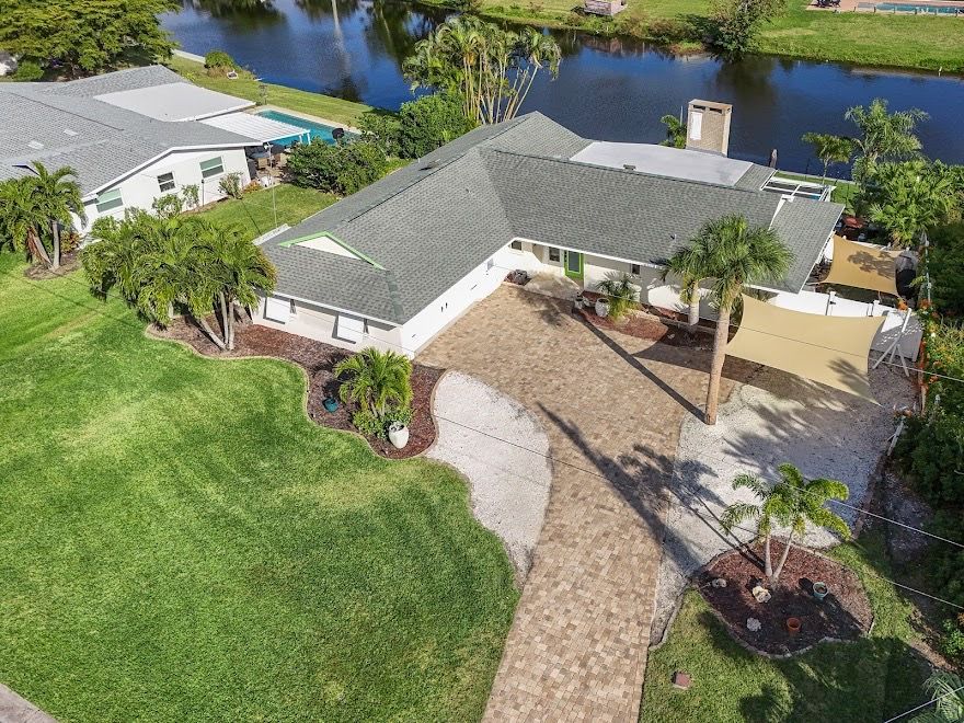 Aerial view of a suburban house with a curved driveway, palm trees, and a canal behind it.