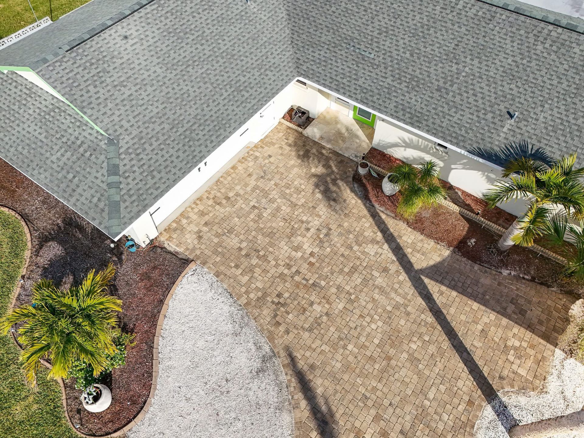 Aerial view of a driveway and front yard with palm trees, gravel, and a house roofline.