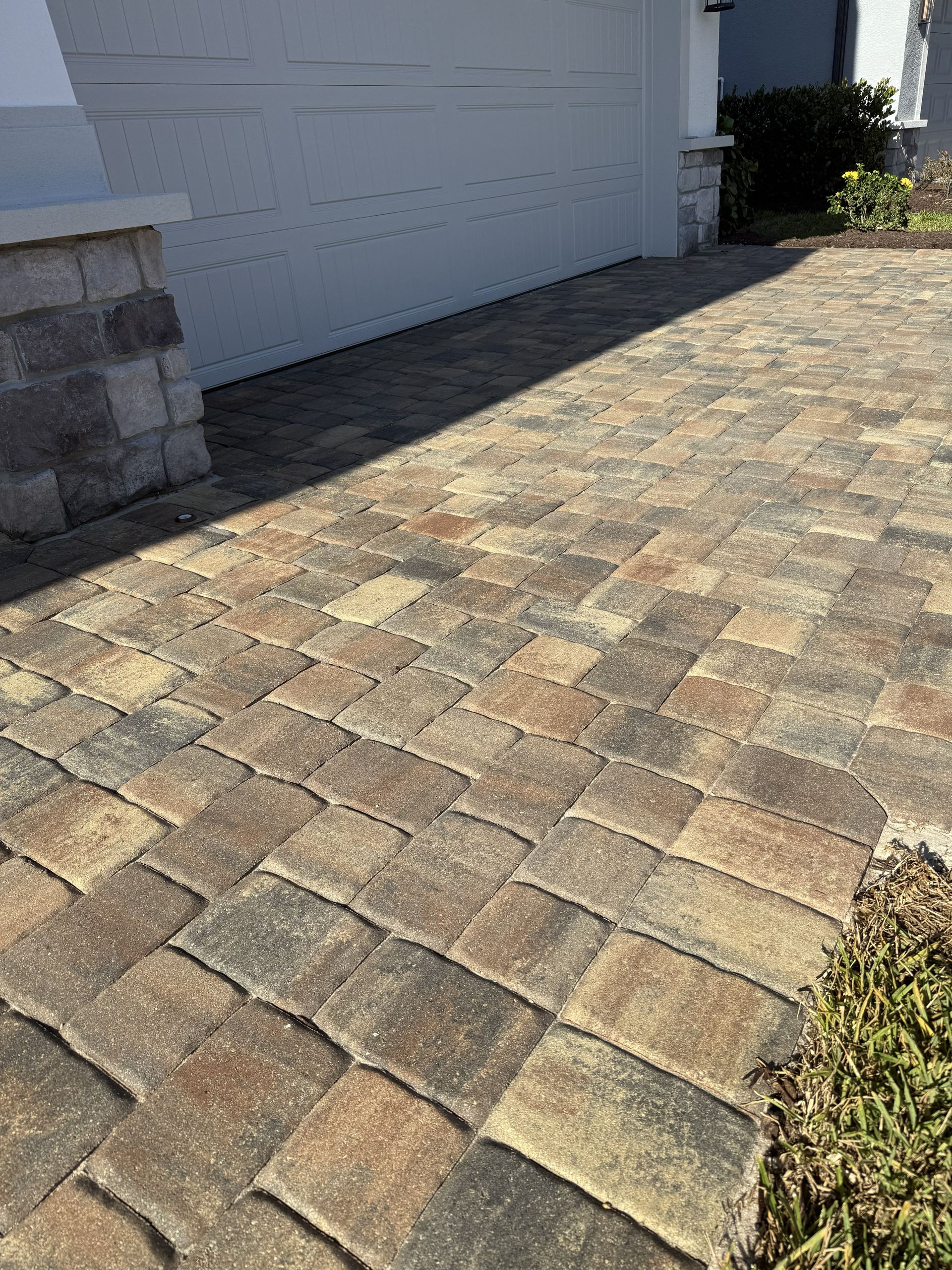 Paver driveway beside a white garage, with sunlit tan and gray stone blocks.