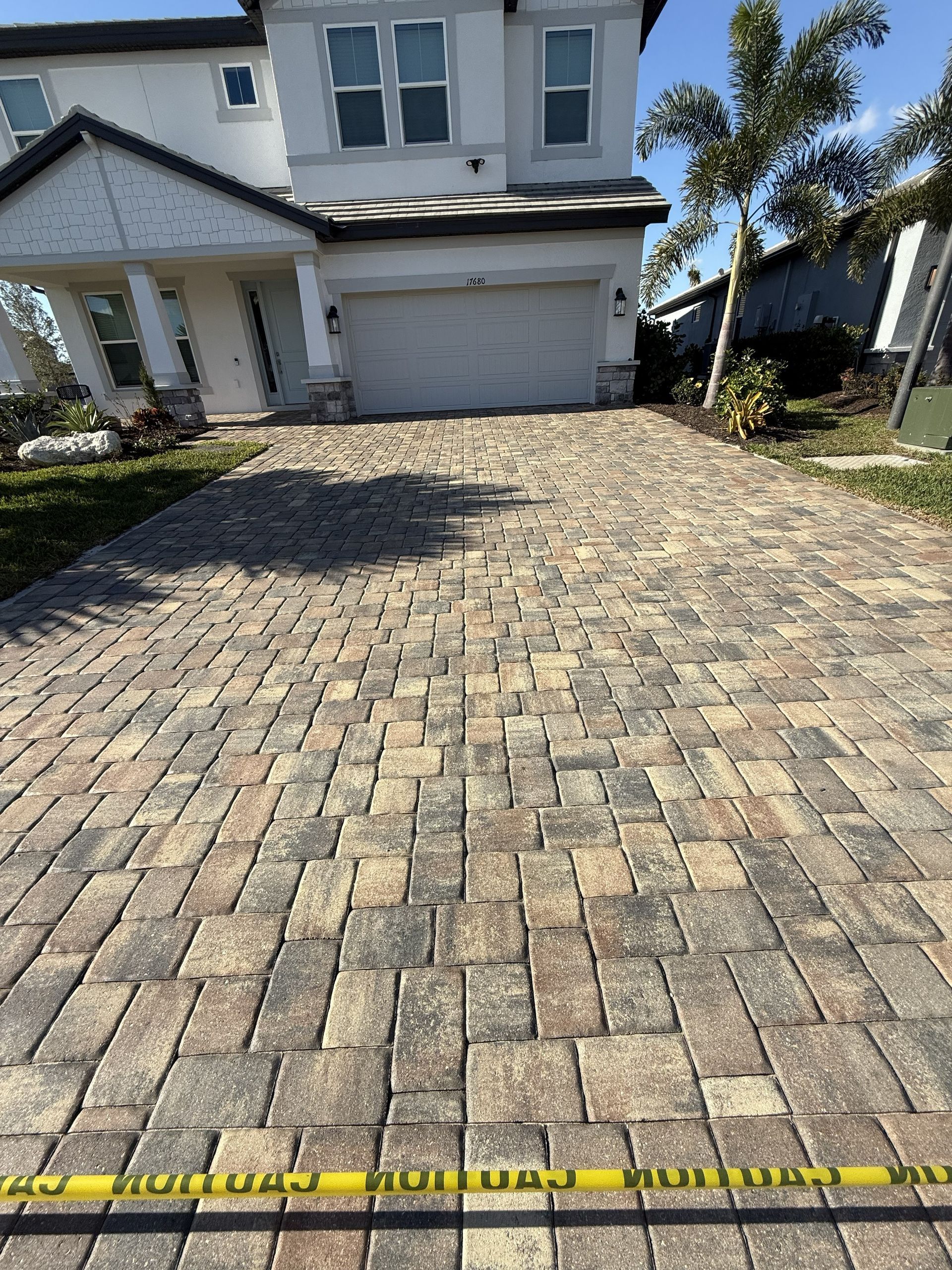 Brick-paved driveway leading to a white garage in front of a house, with a yellow caution tape at the bottom.
