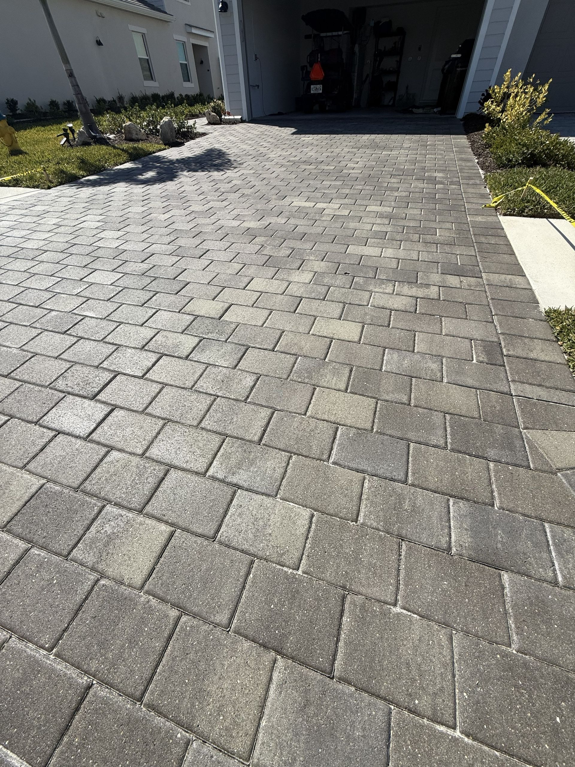 Gray cobblestone driveway leading to a house entrance with landscaping on both sides