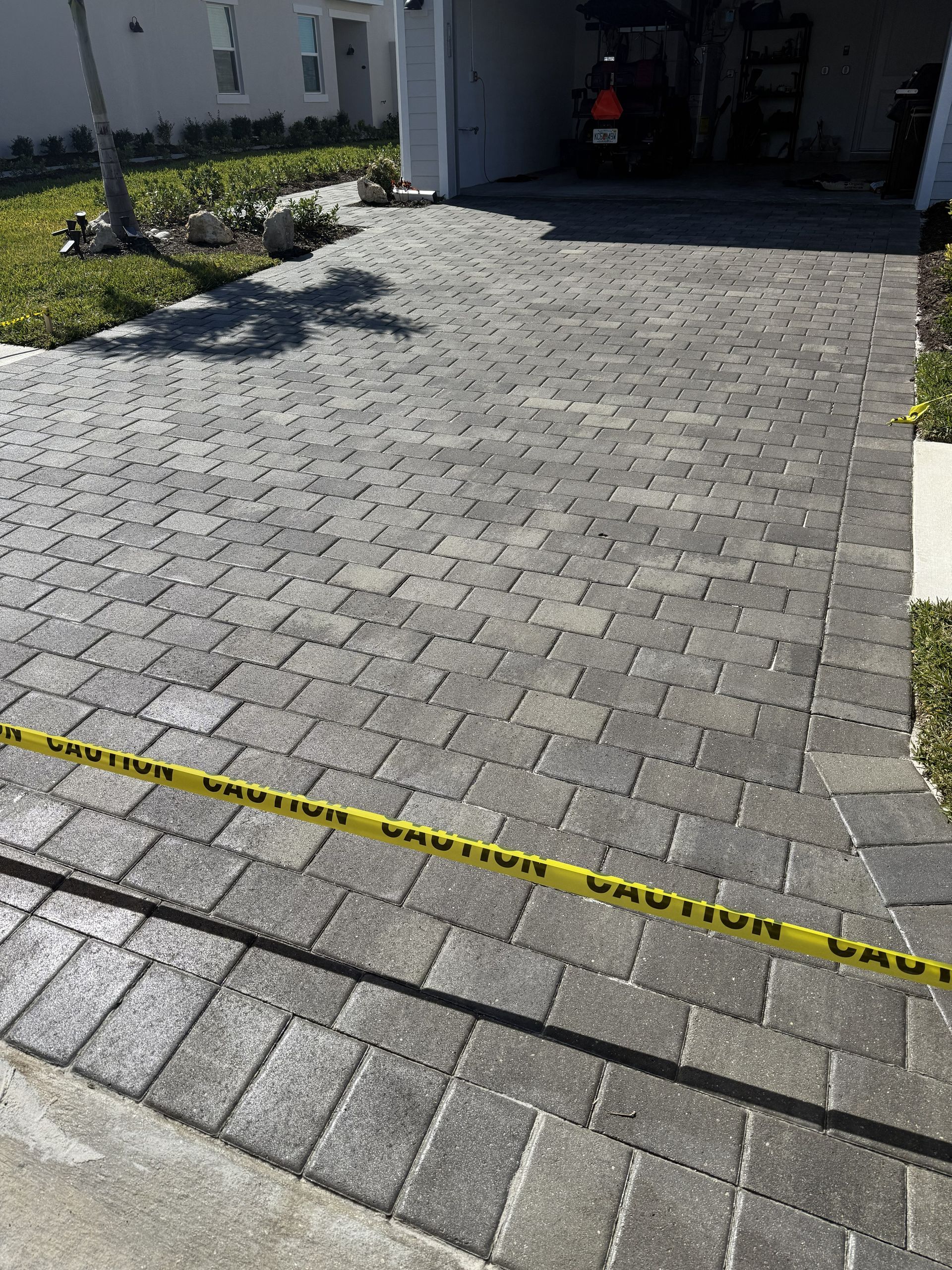 Paver driveway leading to a garage, with yellow caution tape across the bottom edge.