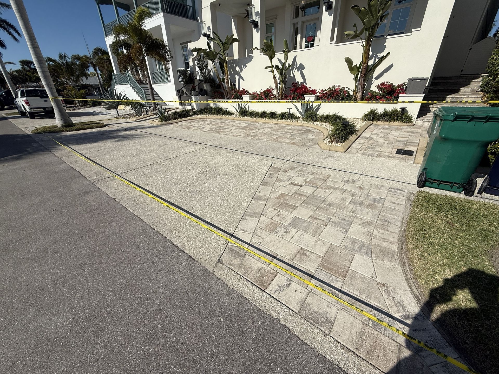 Sloped paved walkway beside a building, with yellow curb line and green trash bin on the right.