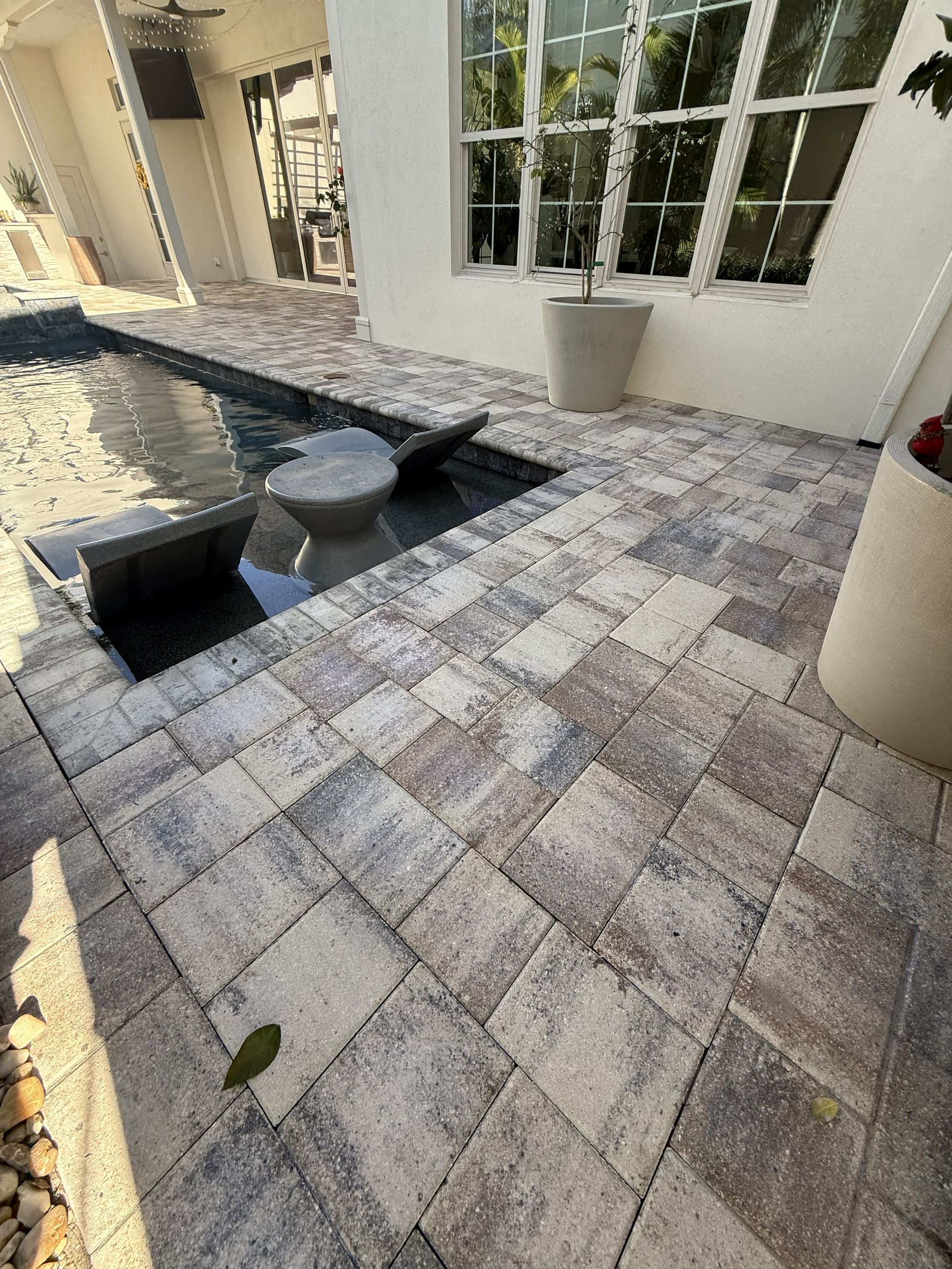 Stone patio with a small black bench, round stool, and white French doors beside a house