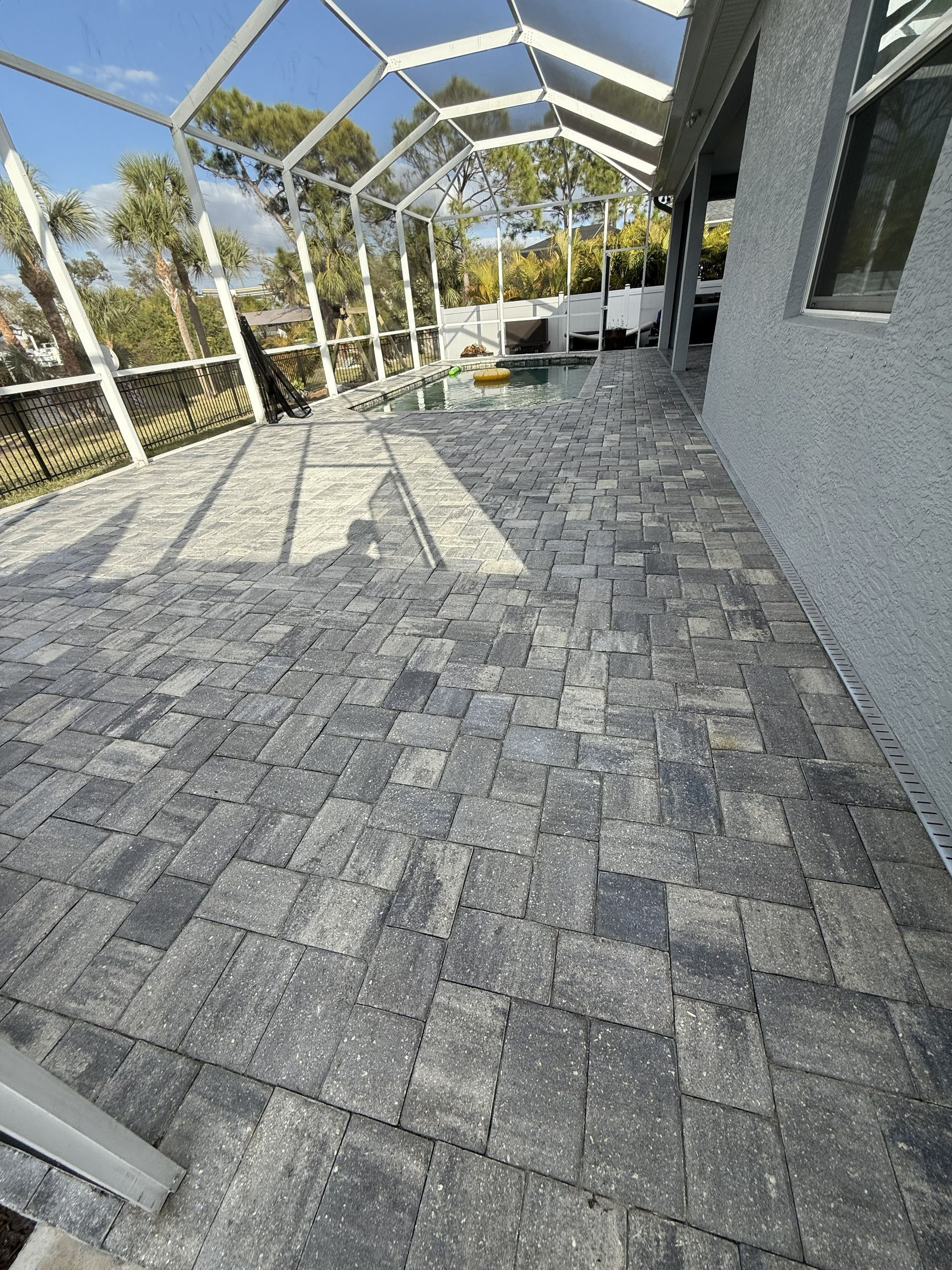 Screened patio with gray pavers, white railing, and outdoor seating in bright sunlight