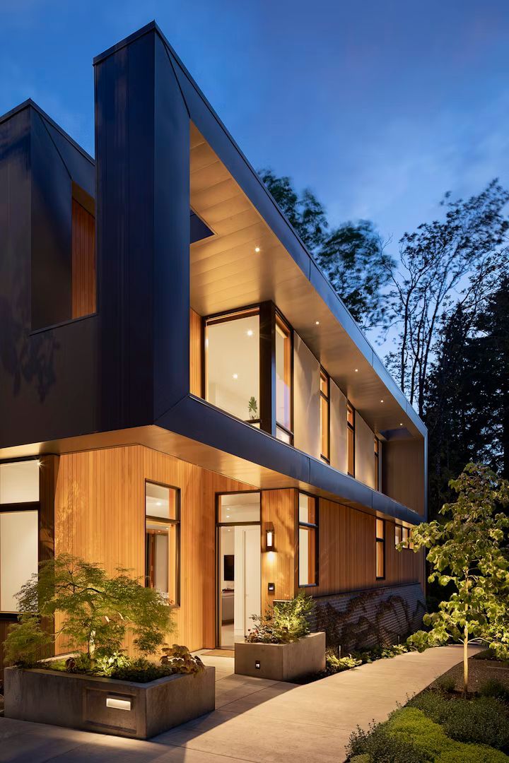 A modern house with a lot of windows is lit up at night.