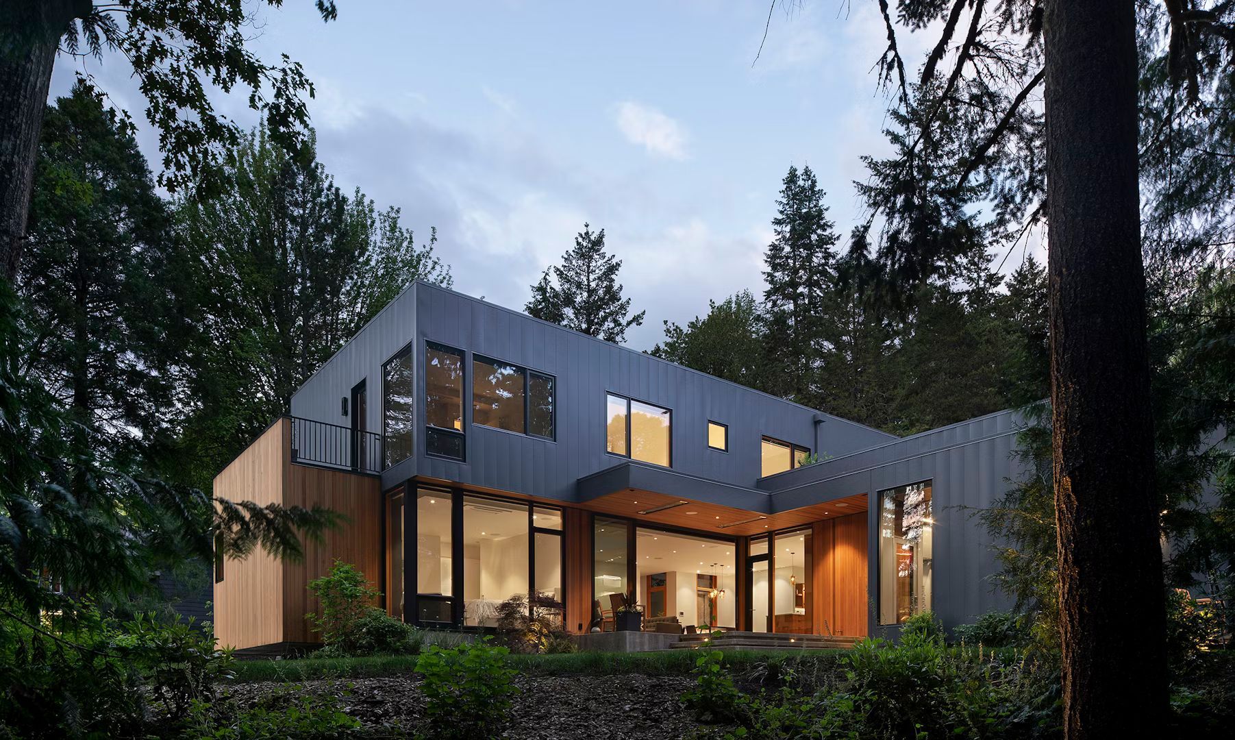 A modern house with a lot of windows is surrounded by trees.