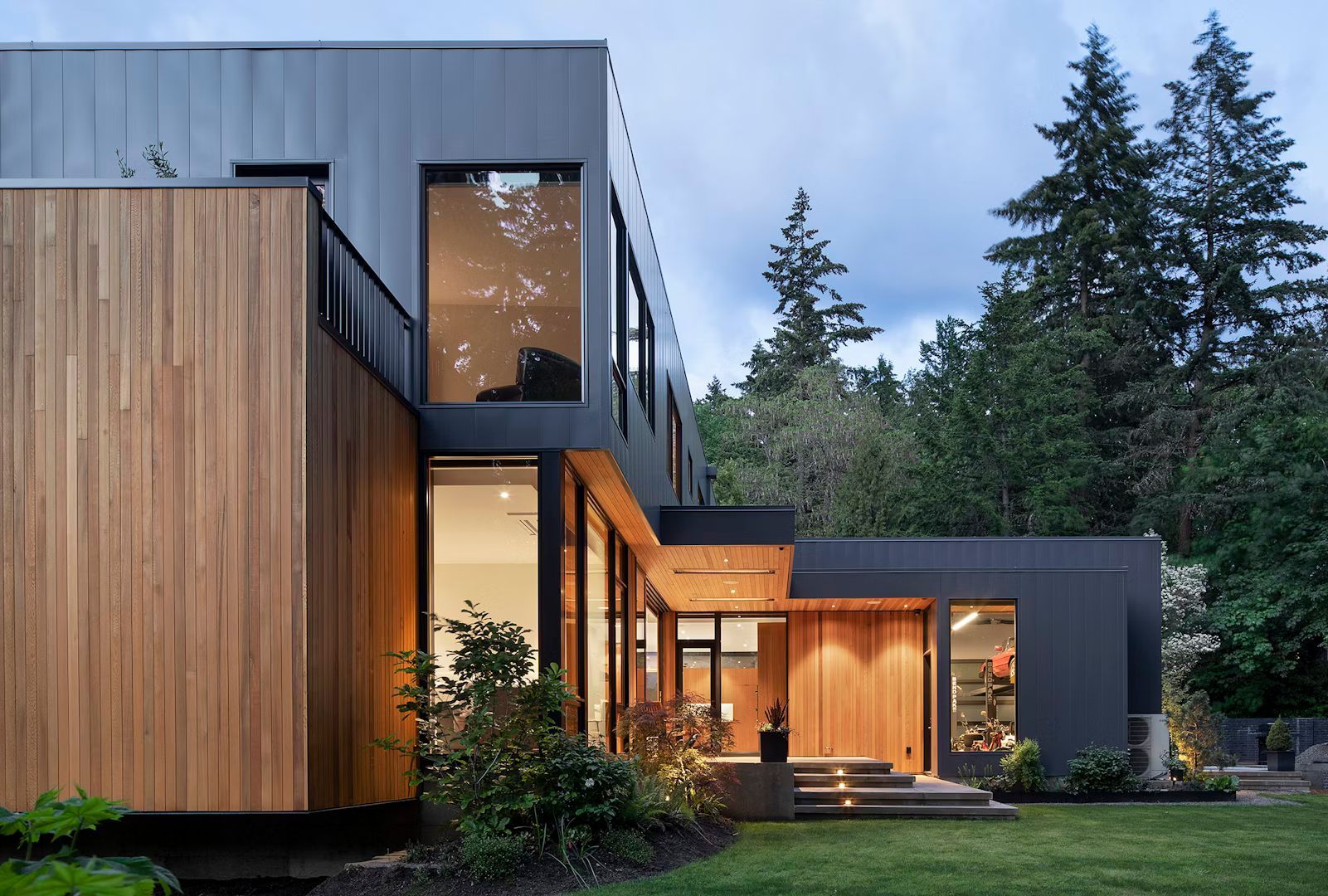 A modern house with a wooden facade and a lot of windows is surrounded by trees.