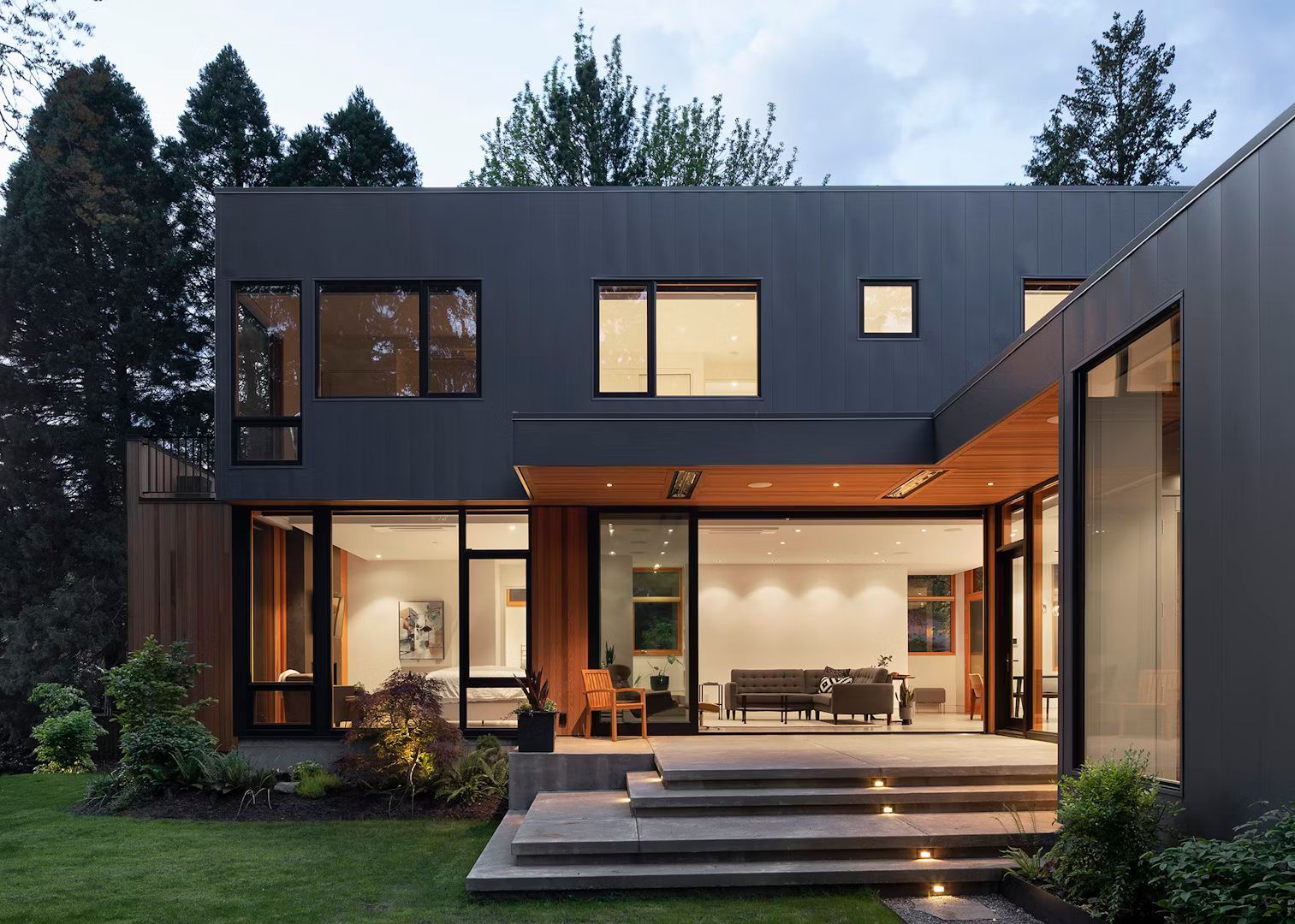 A modern house with a lot of windows is surrounded by trees.