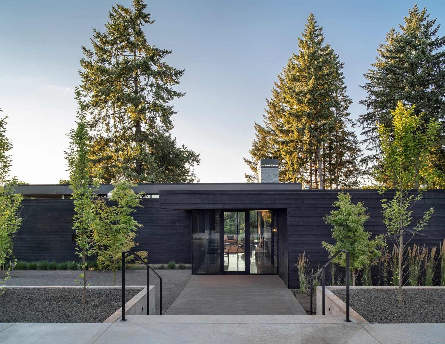 A black house with trees in the background and a walkway leading. to it
