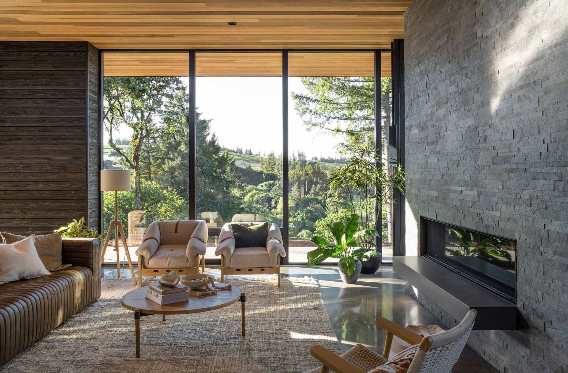 A living room with a fireplace, couch, chairs and a large window.