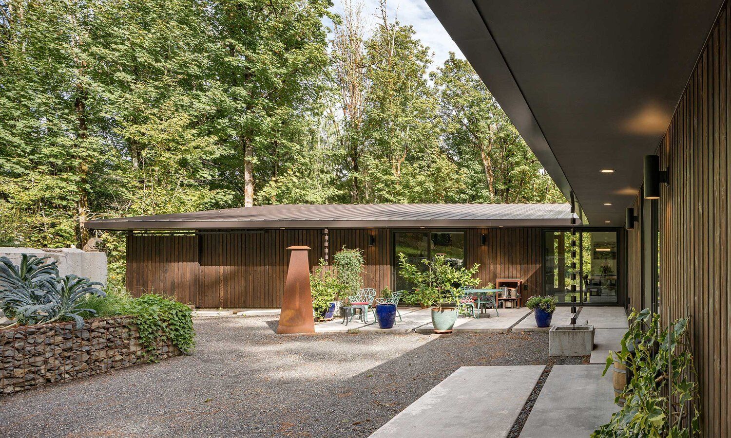 A house with a gravel driveway leading to it is surrounded by trees.