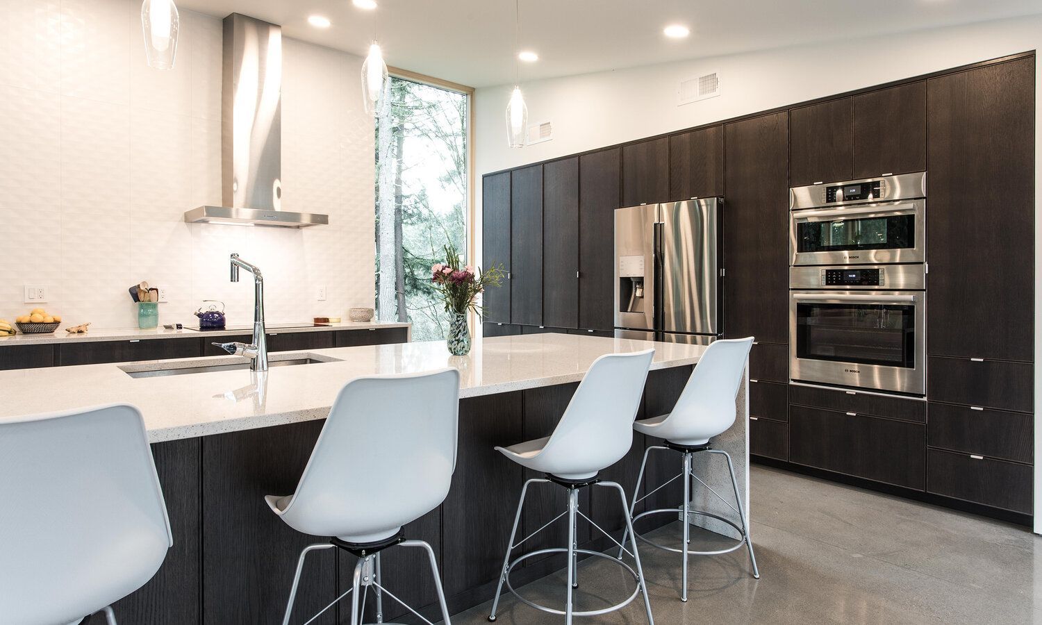 A kitchen with stainless steel appliances and white chairs.