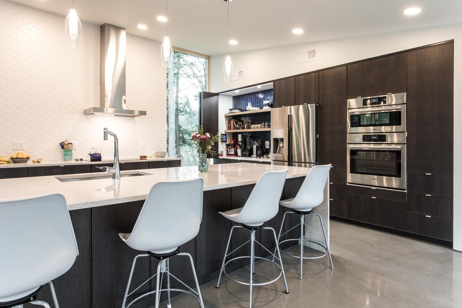 A kitchen with stainless steel appliances and white chairs.