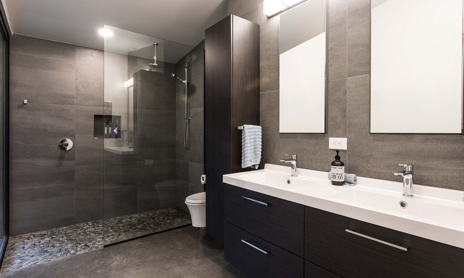 A bathroom with two sinks , a toilet , and a walk in shower.