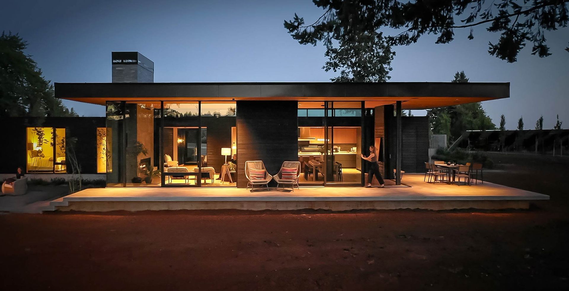 A modern house is lit up at night with people standing outside.