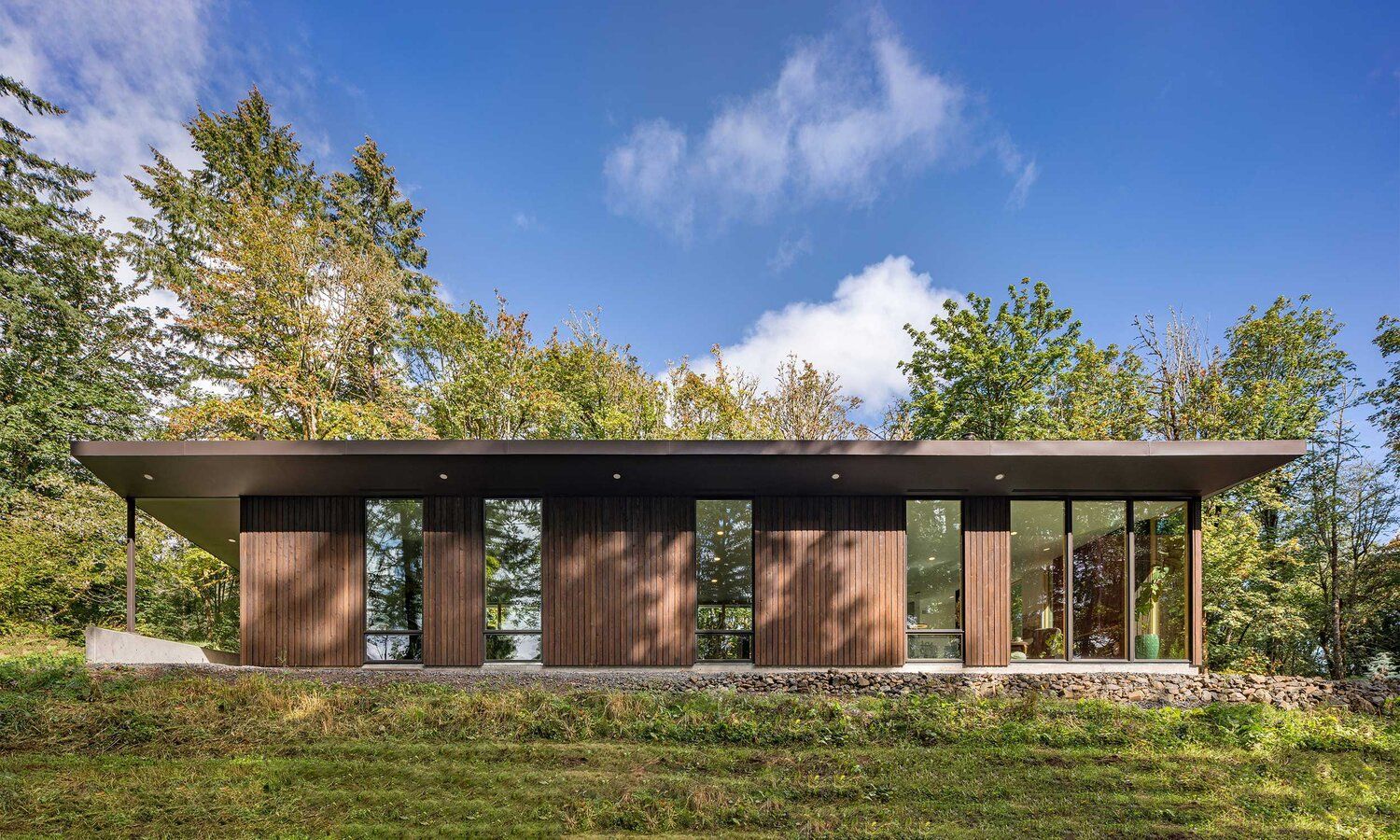 A small house is sitting on top of a grassy hill surrounded by trees.