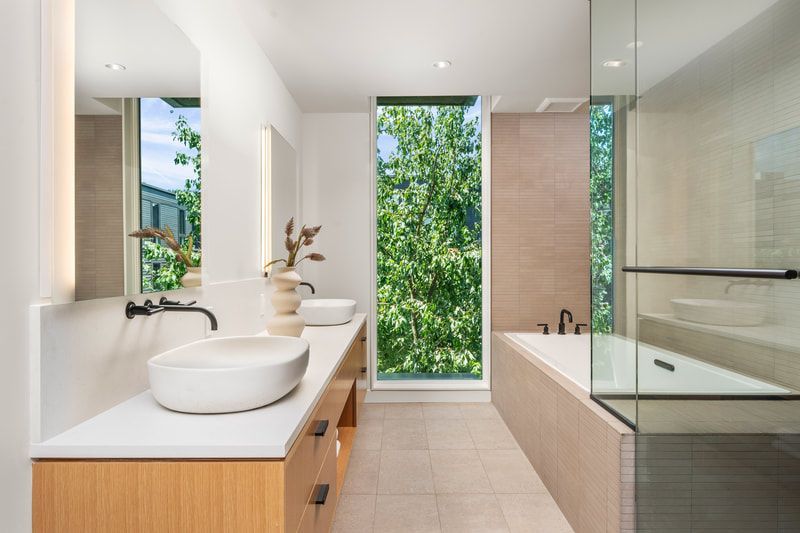 A bathroom with two sinks, a tub, and a window.