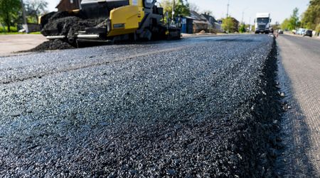 Road paving in progress; asphalt being laid with a yellow paver machine on a sunny day.