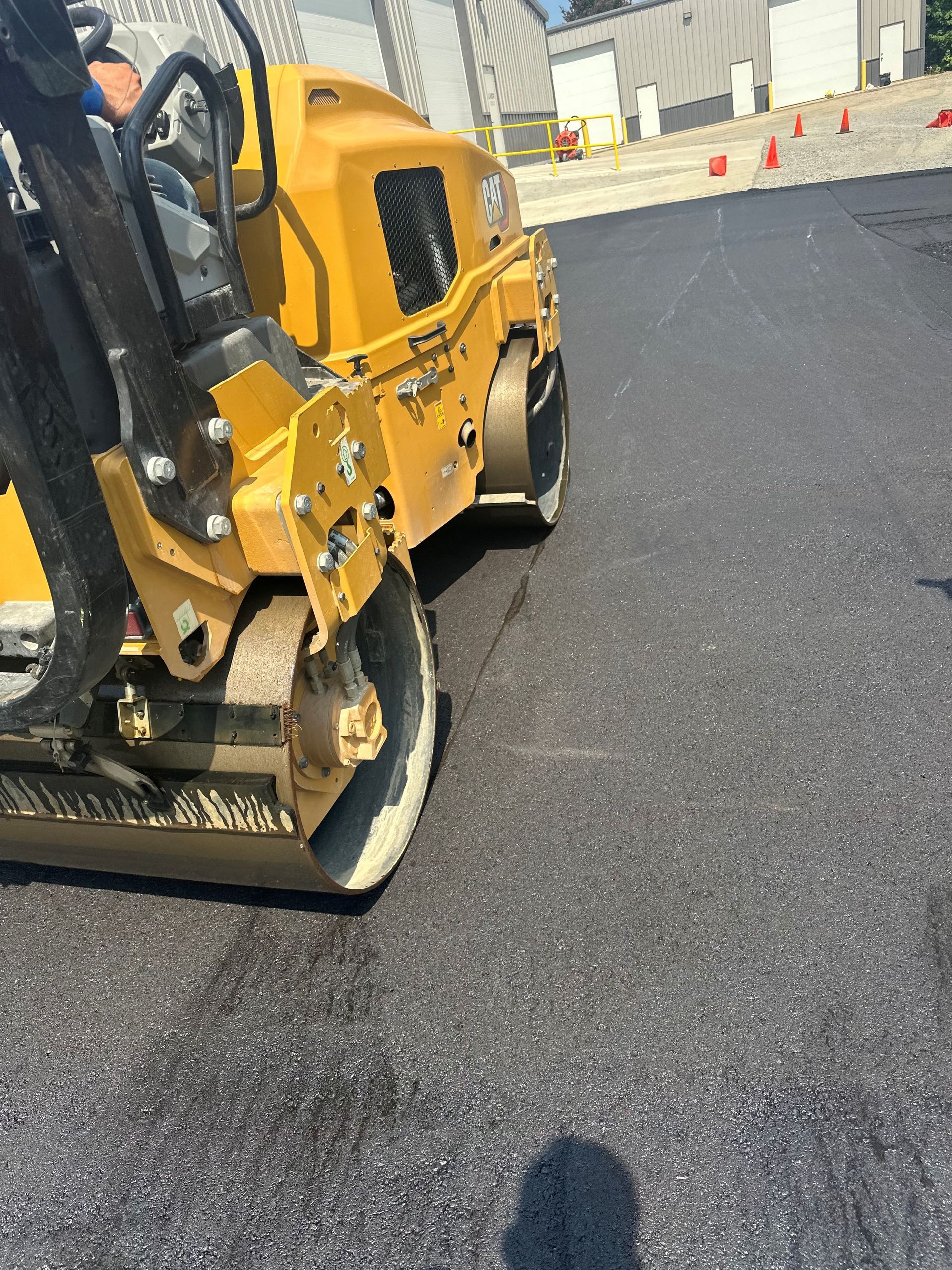 Yellow asphalt roller compacting freshly laid black asphalt on a bright day.