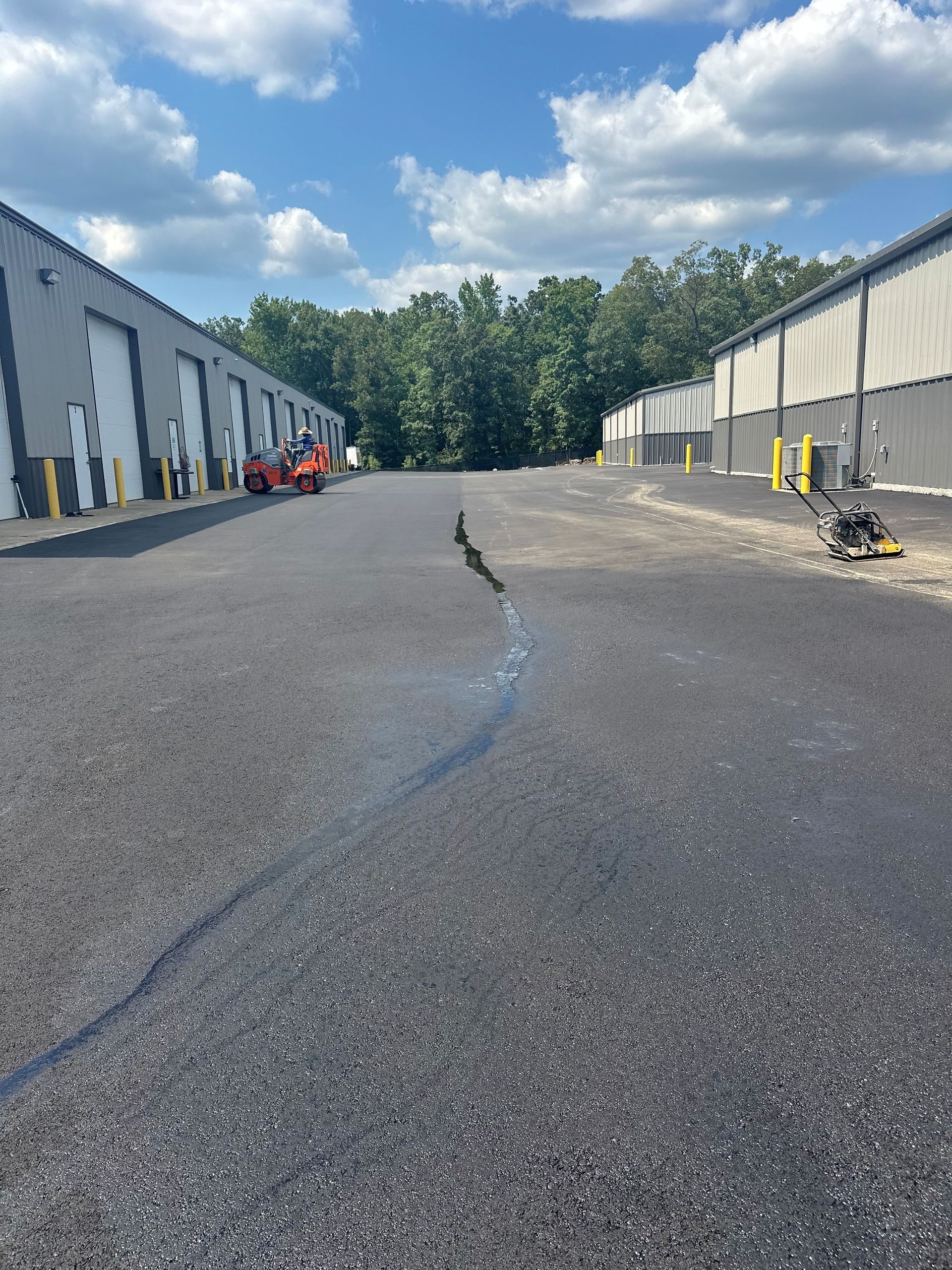 Crack in asphalt parking lot, flanked by industrial buildings under a blue sky.