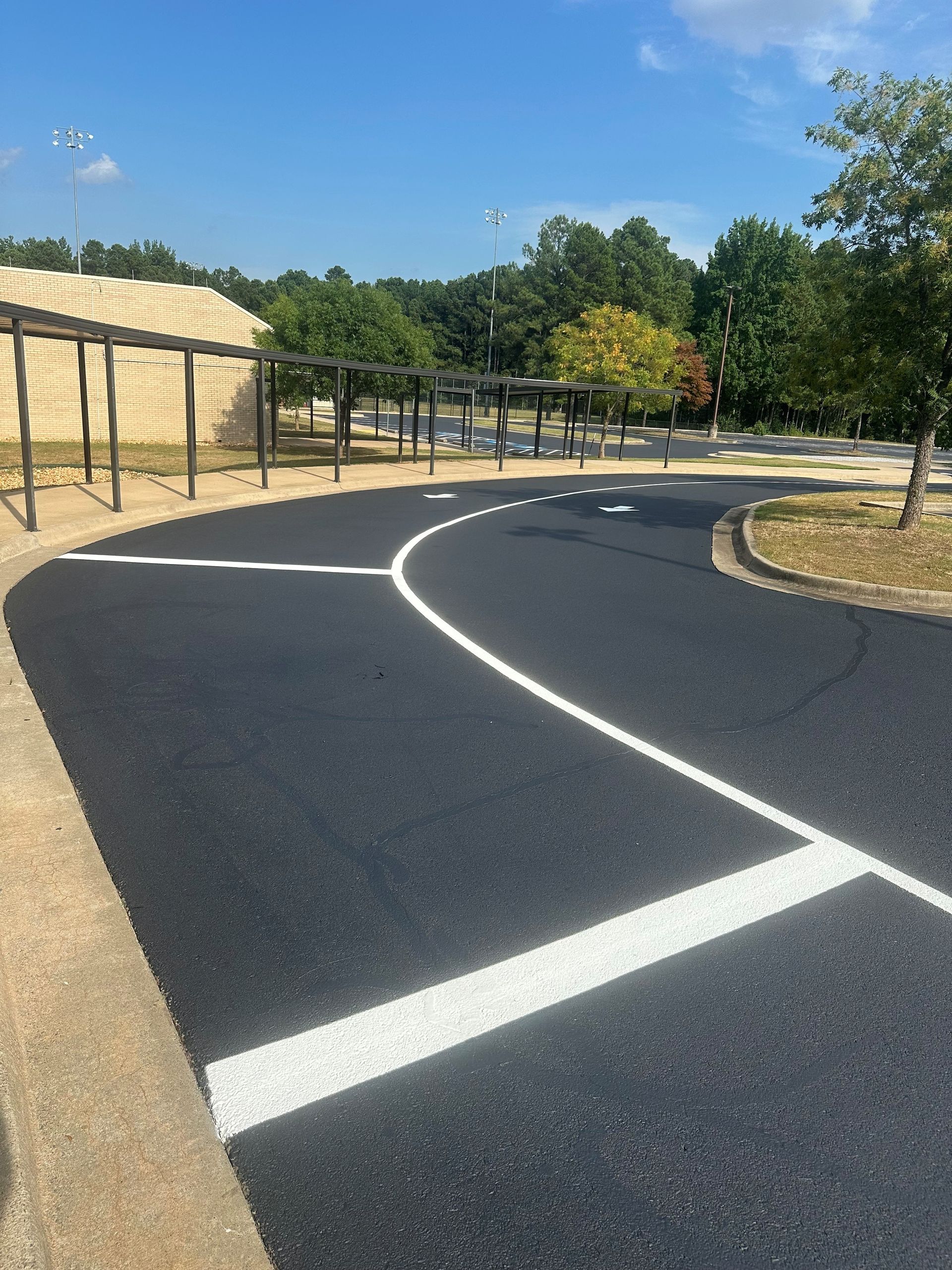 Asphalt road with white lines, next to a building and trees, blue sky.