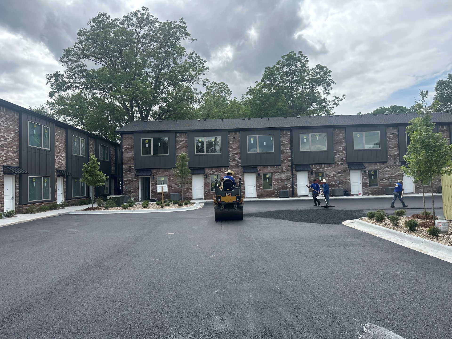 Townhouses with dark brick exteriors, newly paved parking area; construction workers.
