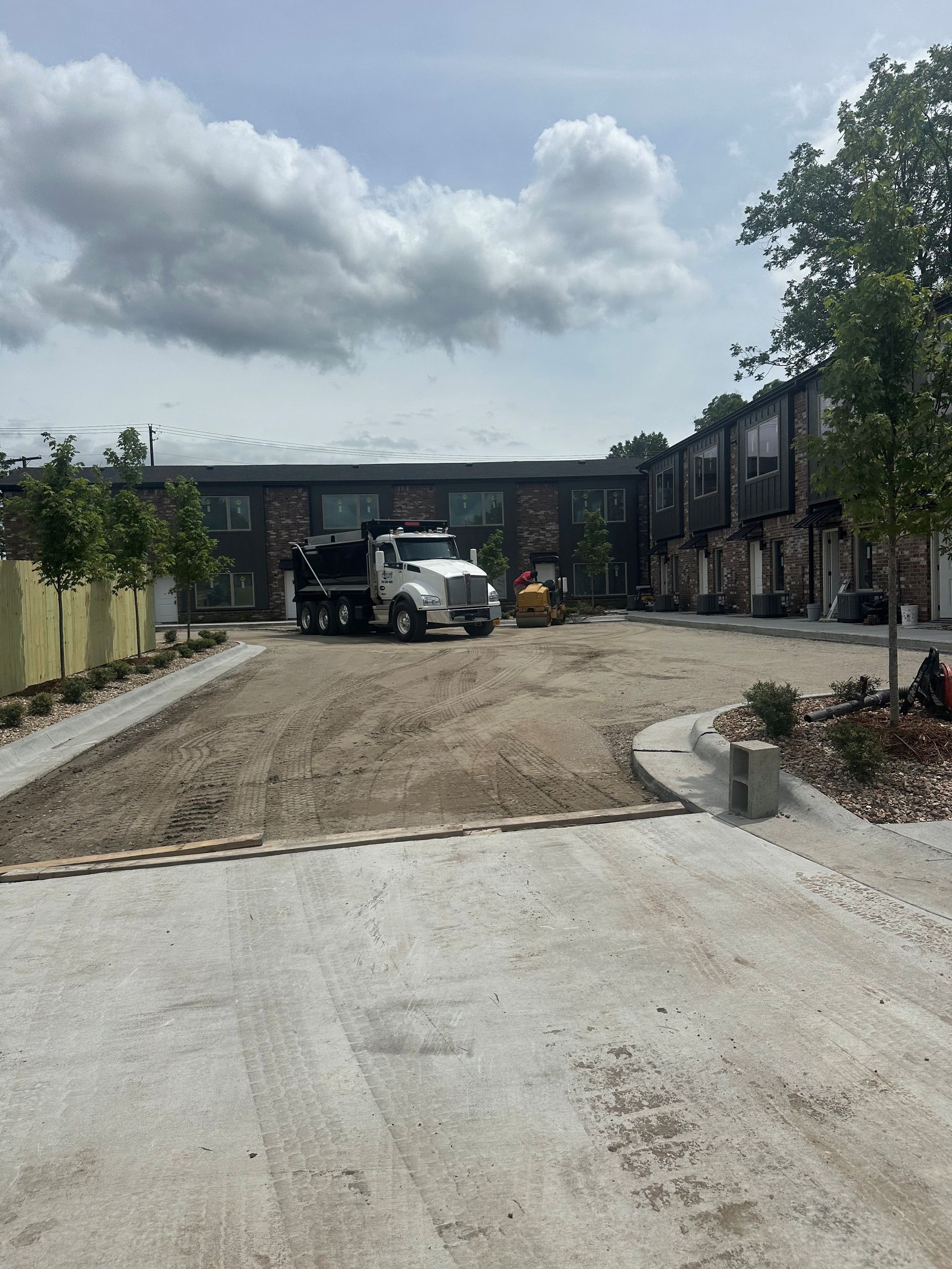 Construction site with dump truck, excavator, and building.  Dirt road and curb.
