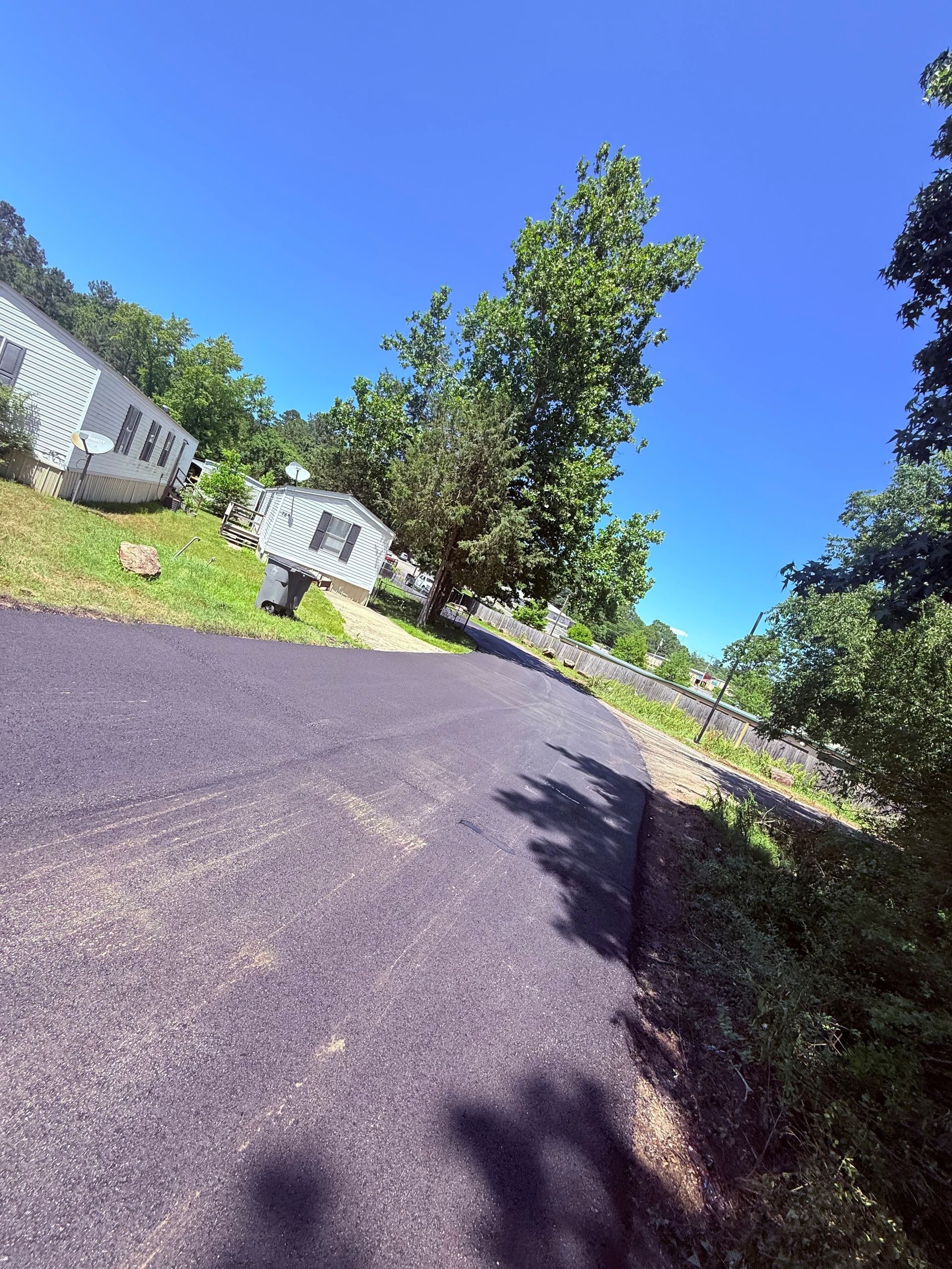 Asphalt road leading uphill toward small buildings on a sunny day.