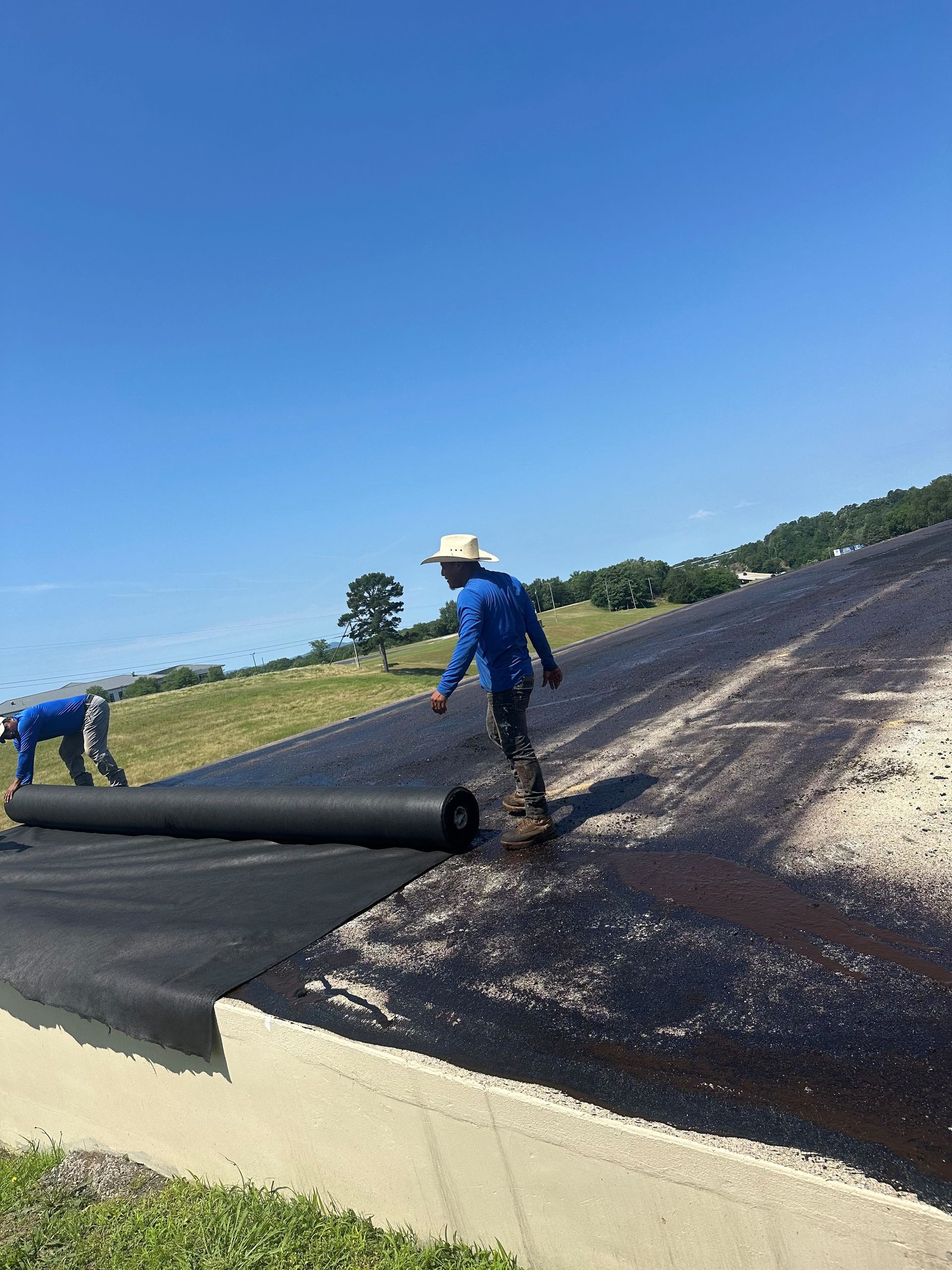 Two workers rolling out black fabric on asphalt. Sunny day.