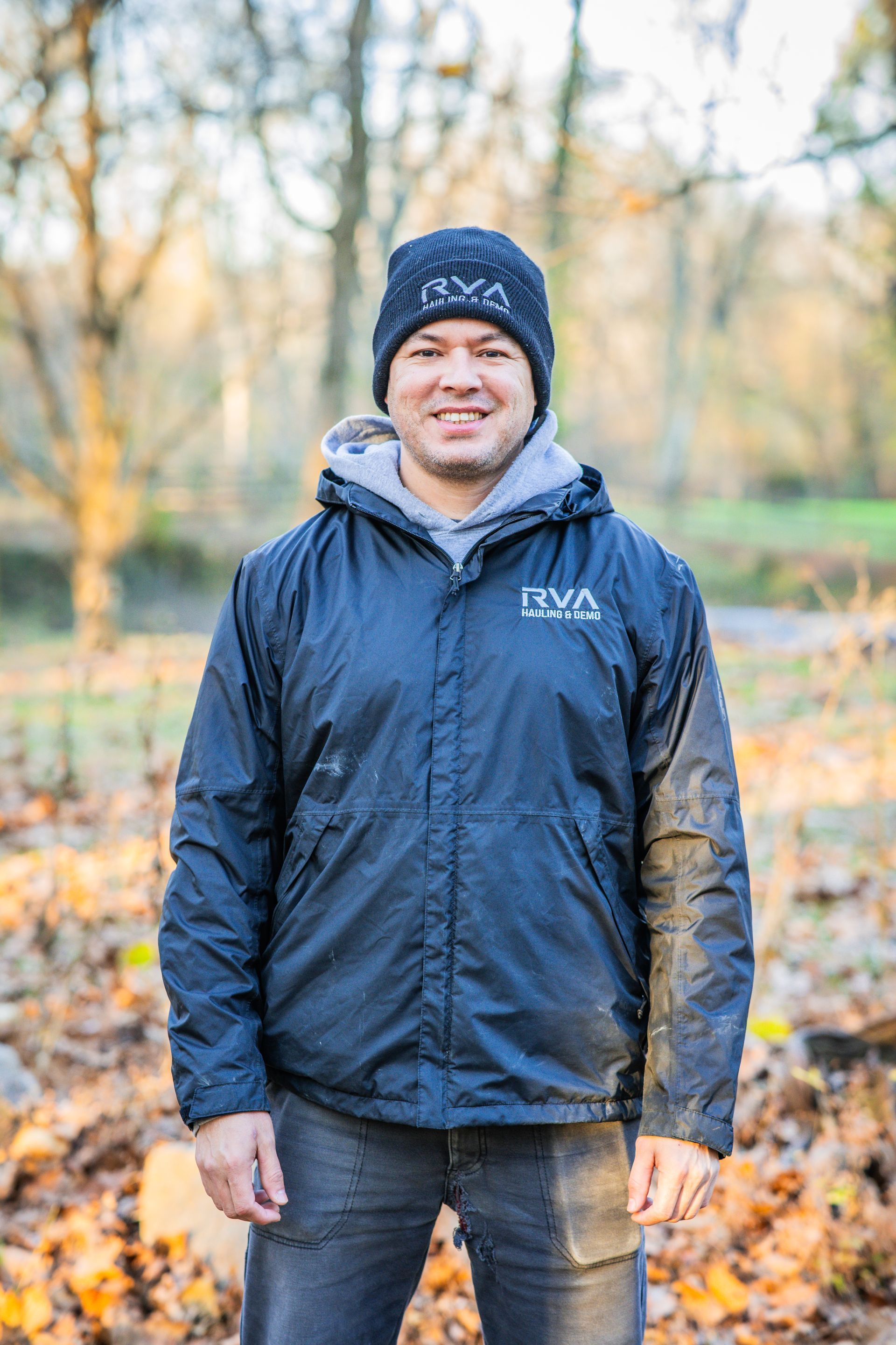 Man in dark jacket and beanie smiles outdoors.