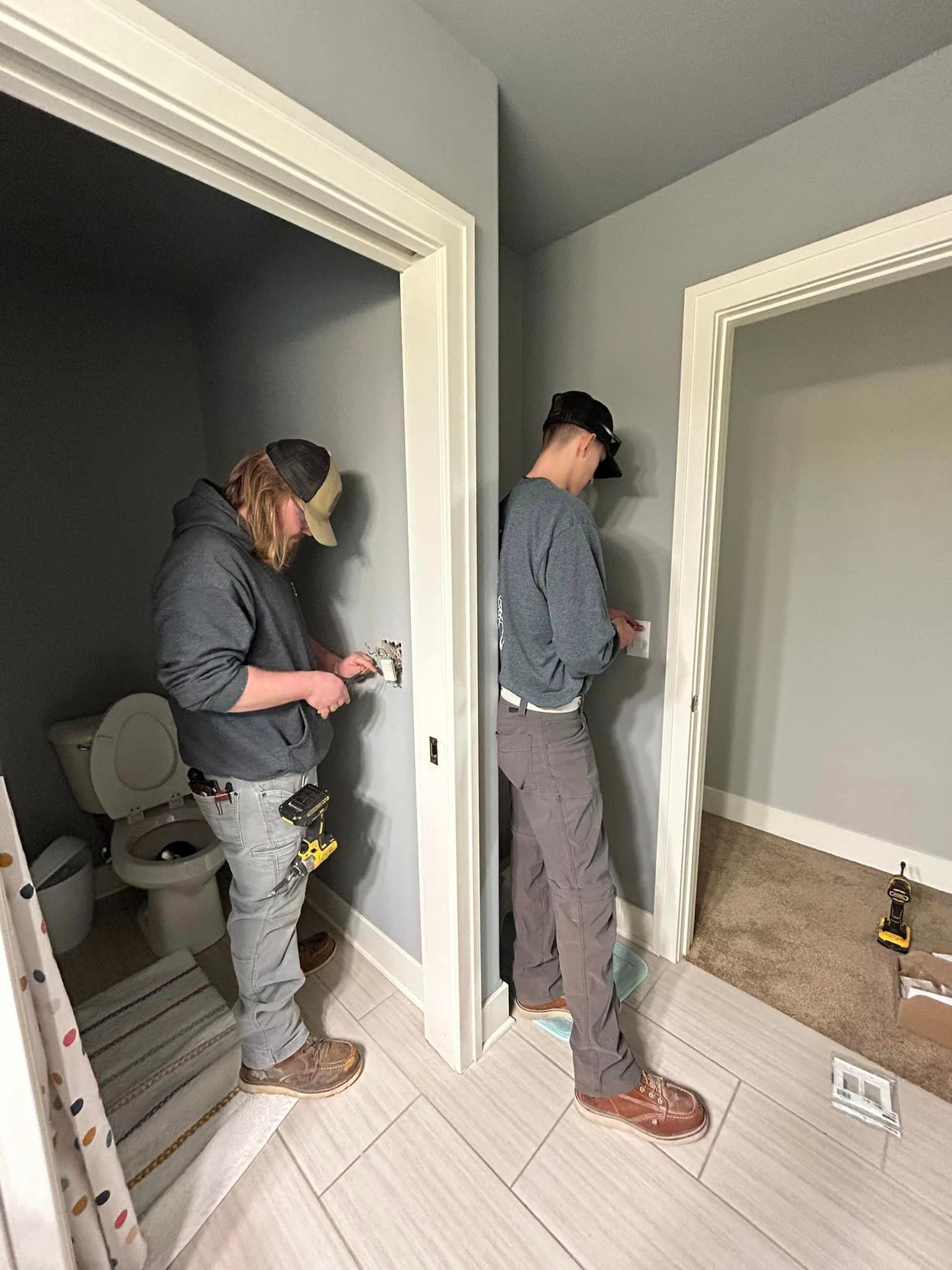 Two men are working on a bathroom's electrical wiring