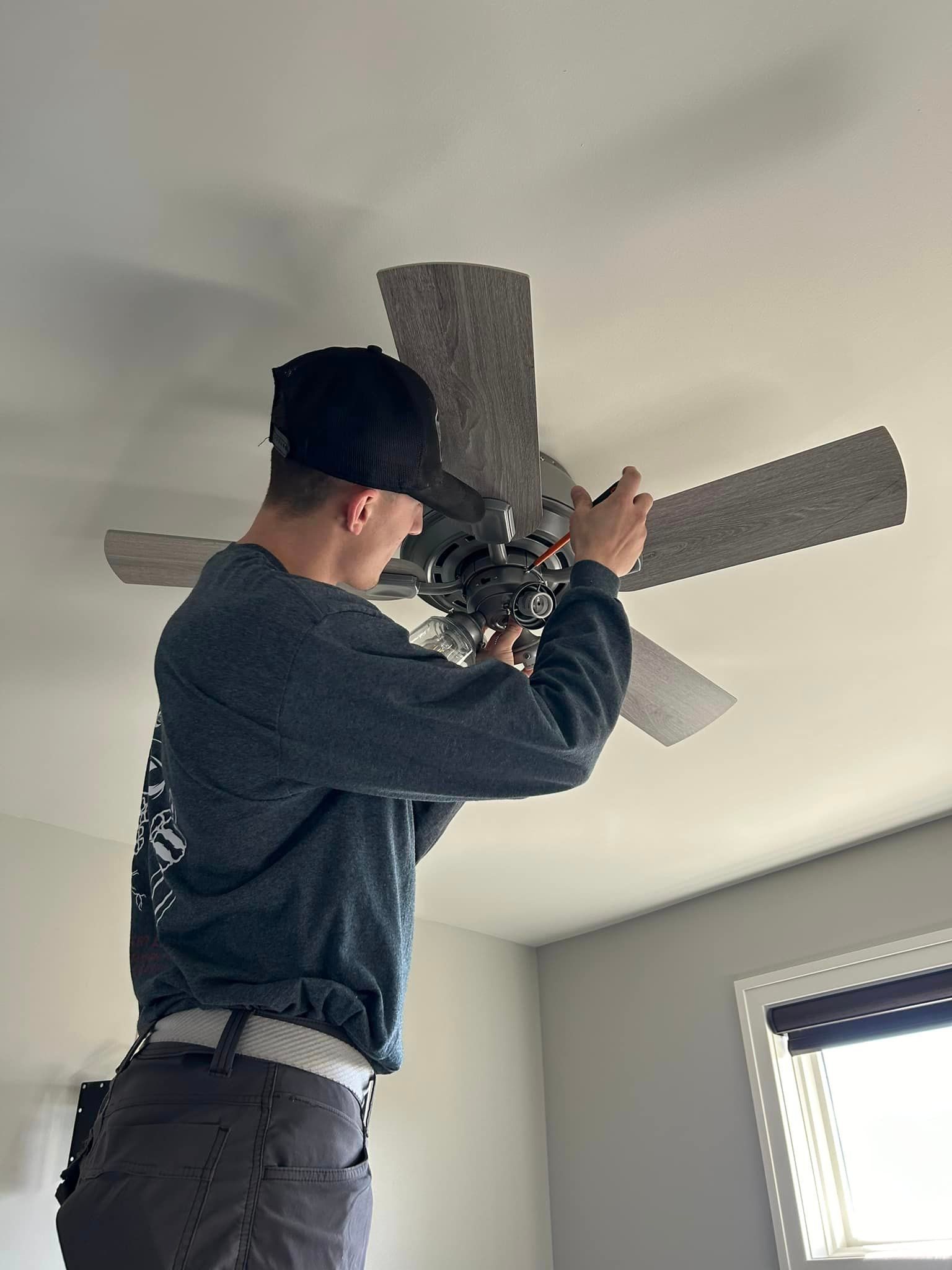A man is in the process of installing the electrical wiring for a ceiling fan