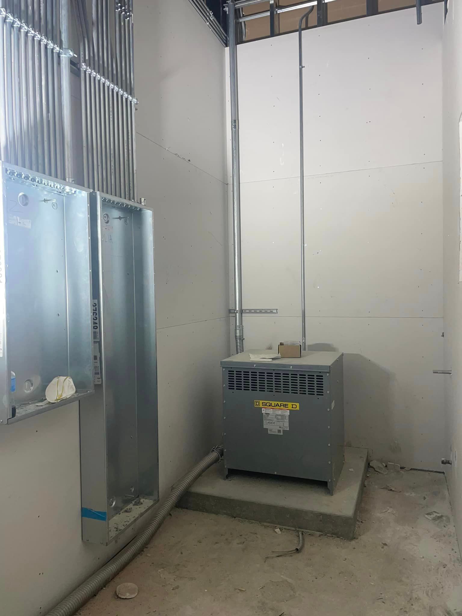 A transformer is sitting in a room next to an electrical panel frame