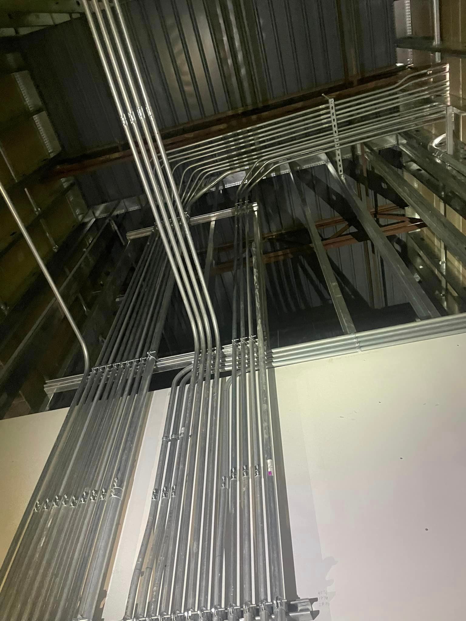 A bunch of electric metallic tubes are hanging from the ceiling of a building