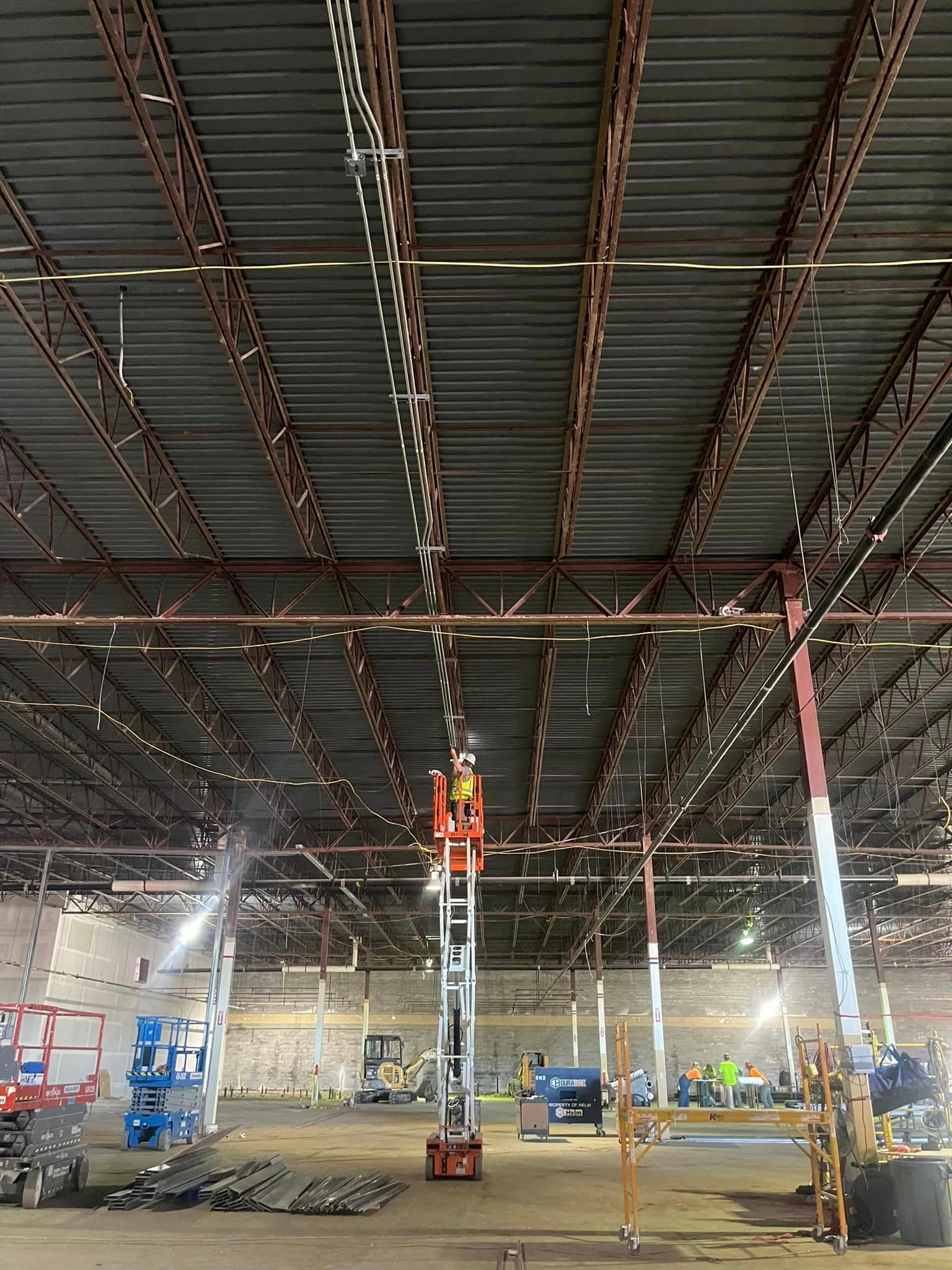 A man is standing on a scissor lift in a large industrial facility