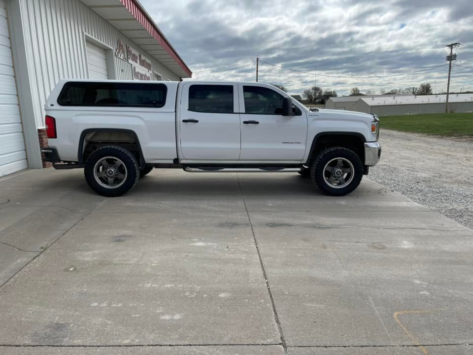 A white truck with a canopy is parked in front of a garage
