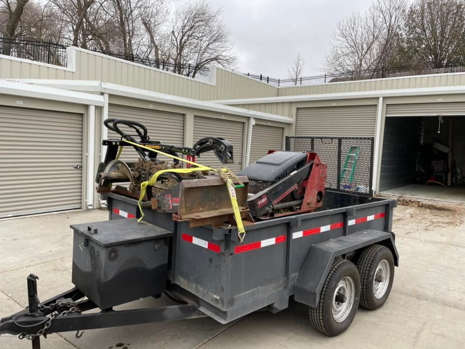 A trailer with a tractor on it is parked in front of a garage