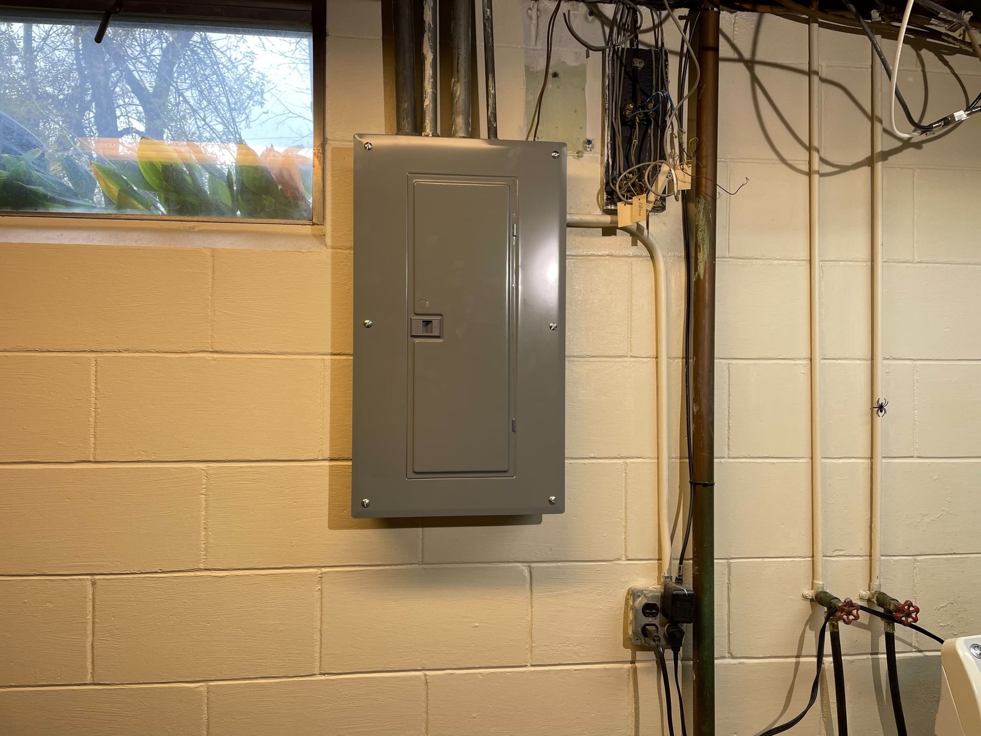 A gray electrical box is installed on a brick wall in a basement