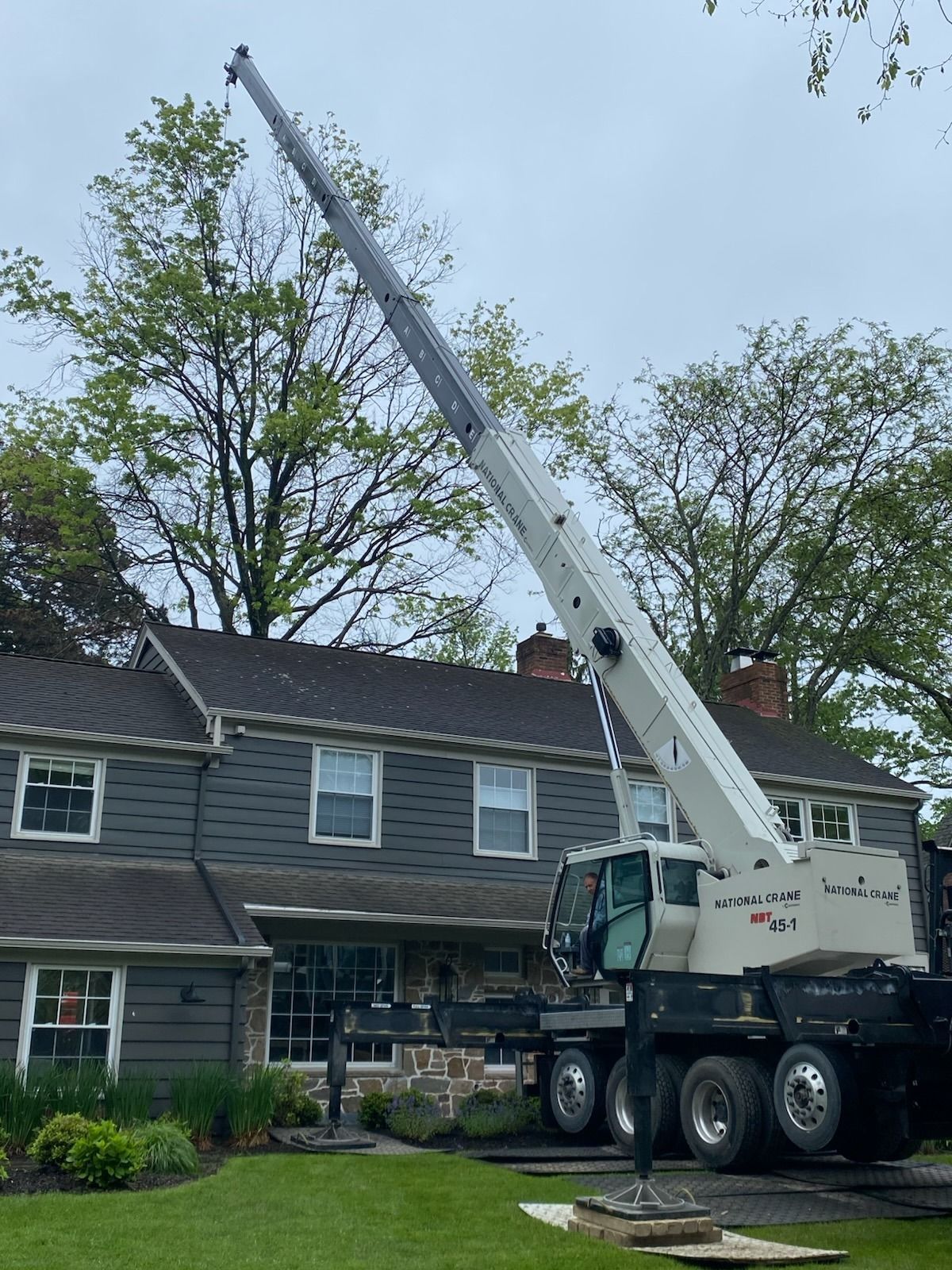 A large white crane extends over a two-story house, possibly for construction or repair work.