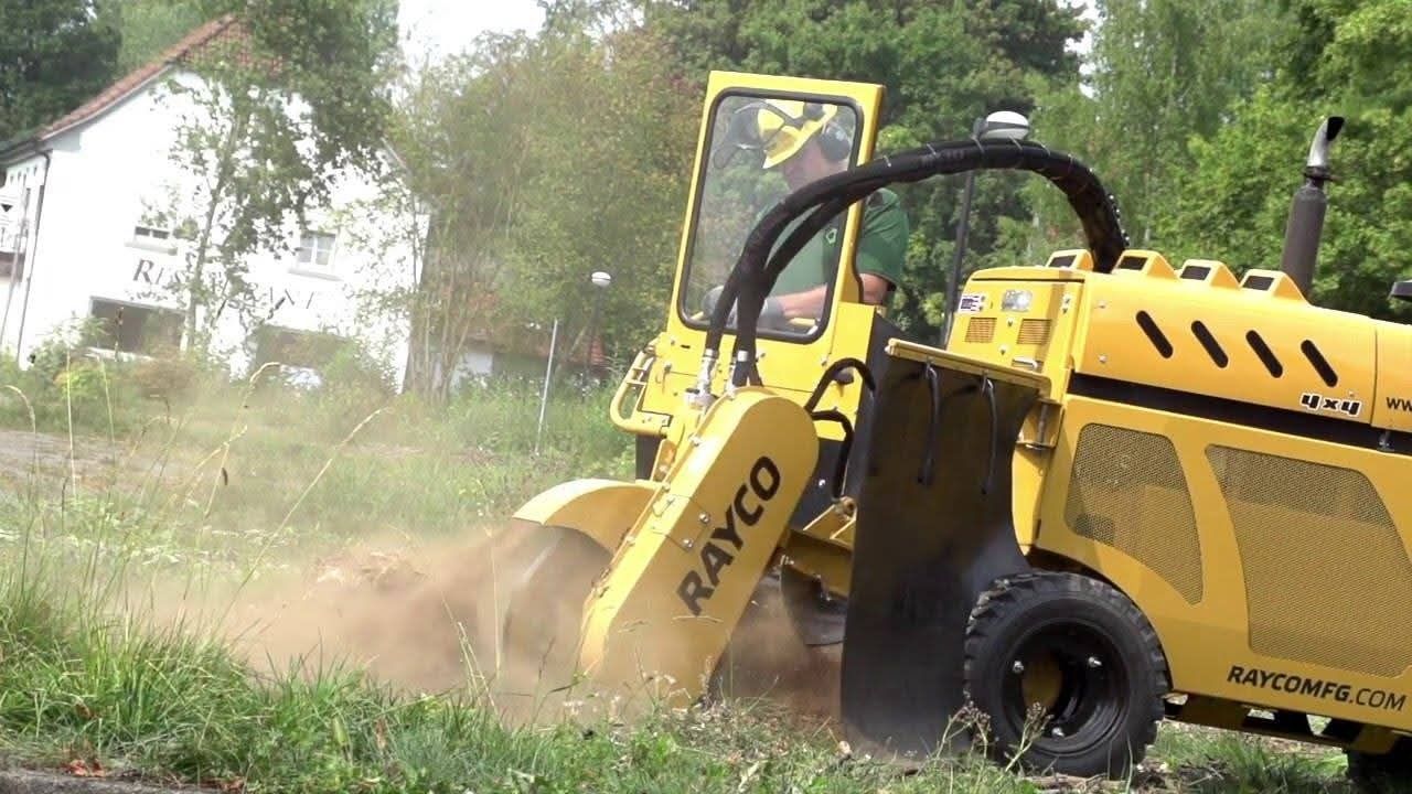 Yellow stump grinder, operated by a person, grinding a tree stump in grassy area.