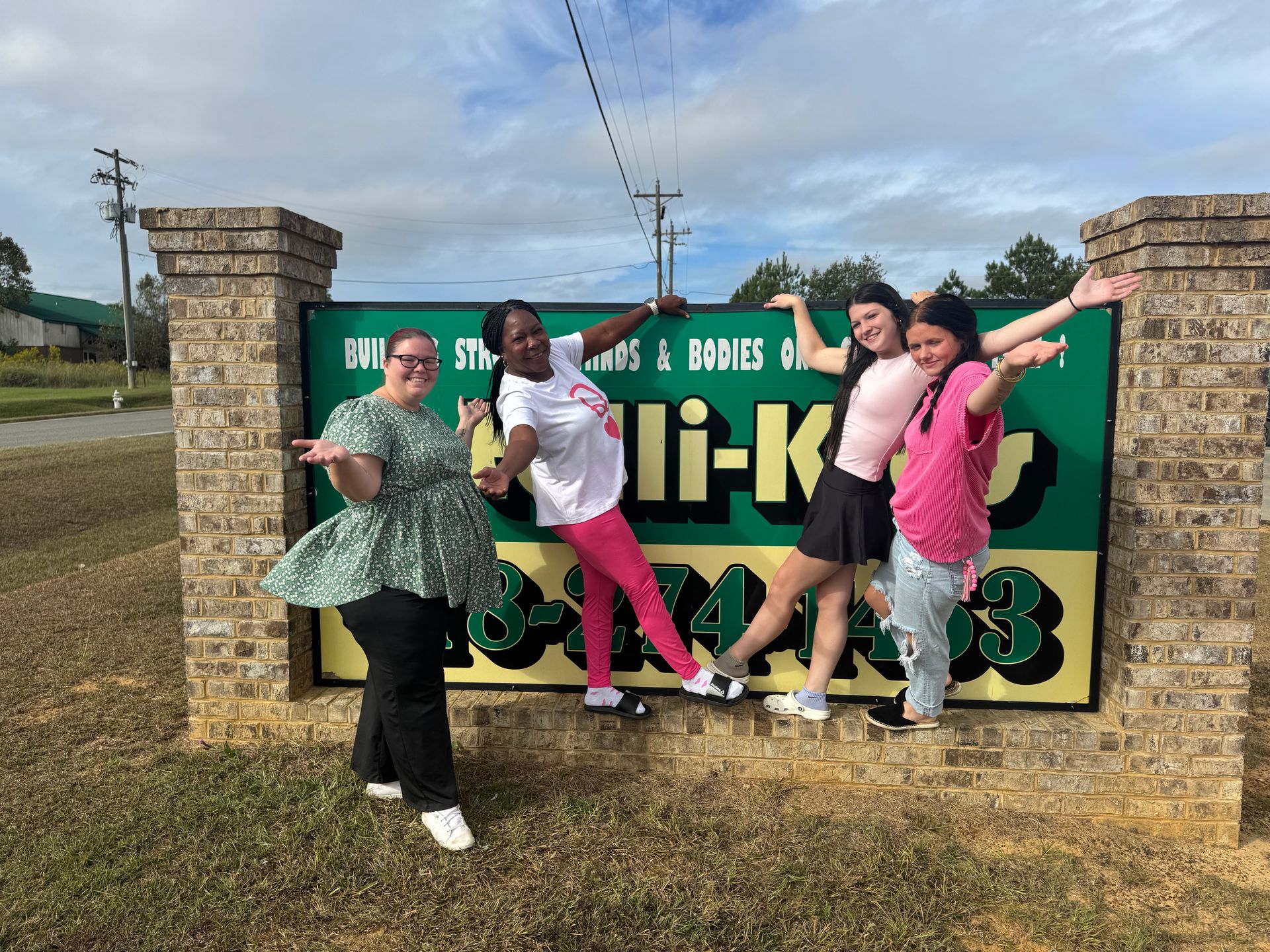 Four people posing in front of a green sign with a business name and phone number on it.