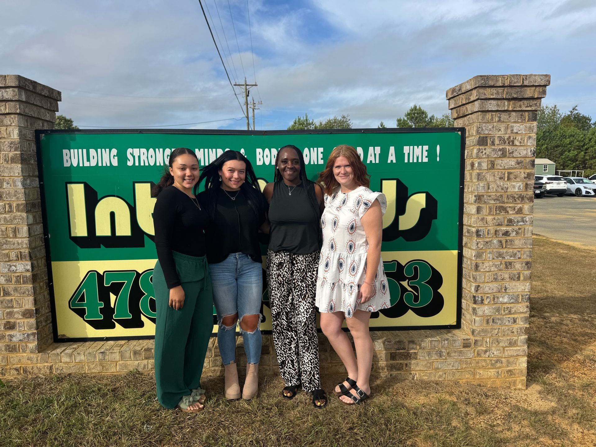 Four people stand in front of a green sign that says 