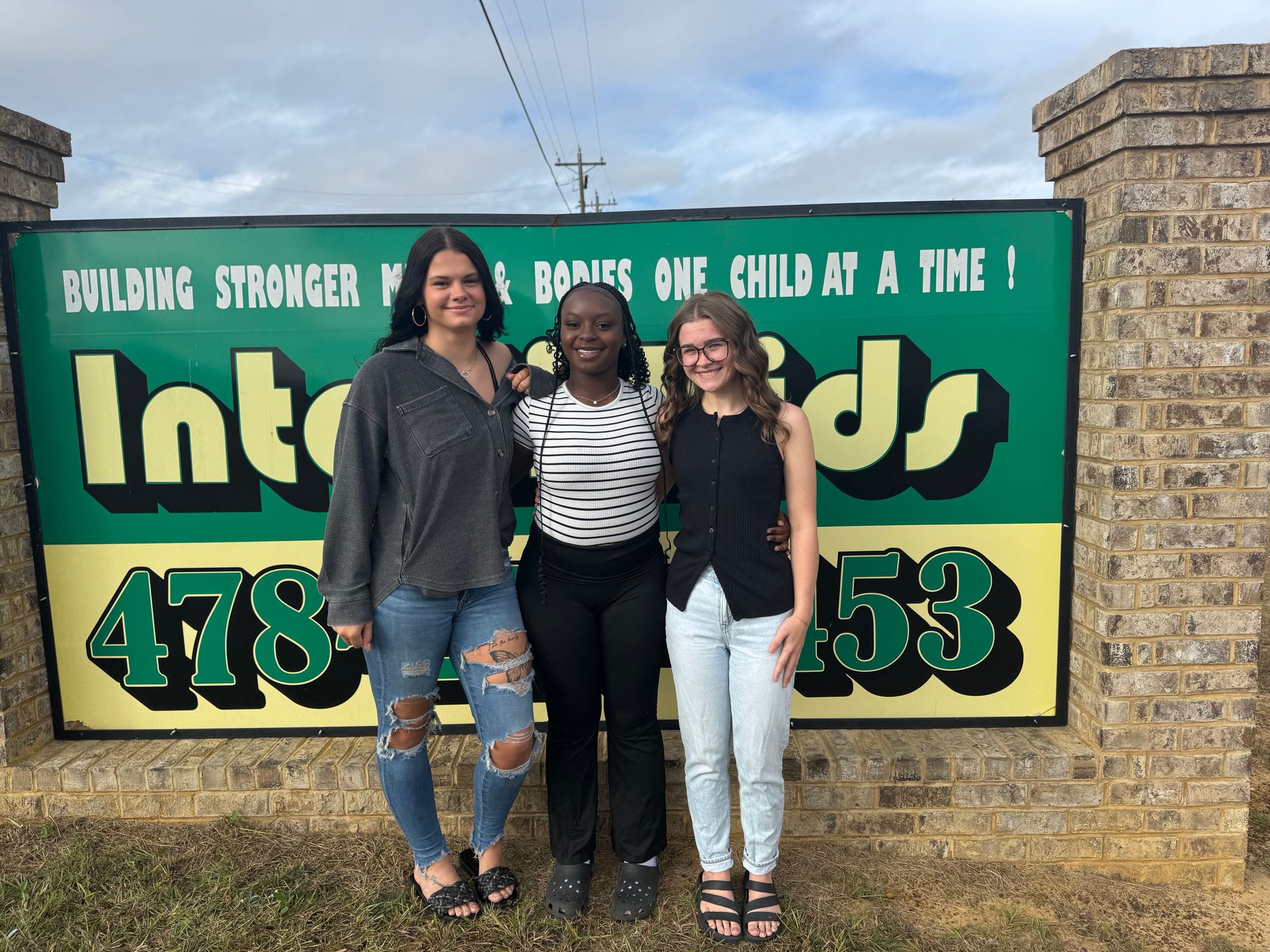 Three people standing in front of a green sign.
