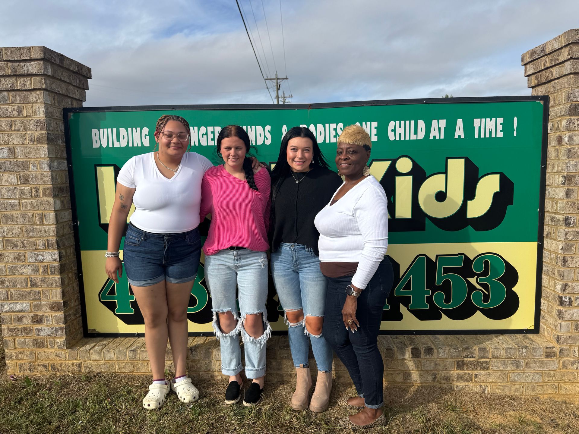 Four people stand in front of a daycare sign.