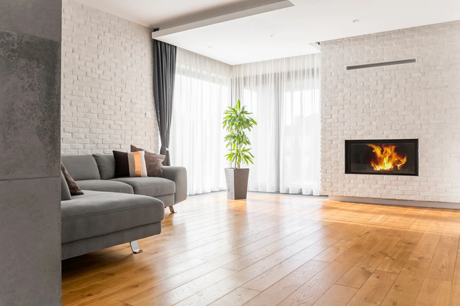 Modern living room with fireplace, gray sofa, brick walls, and hardwood floors.