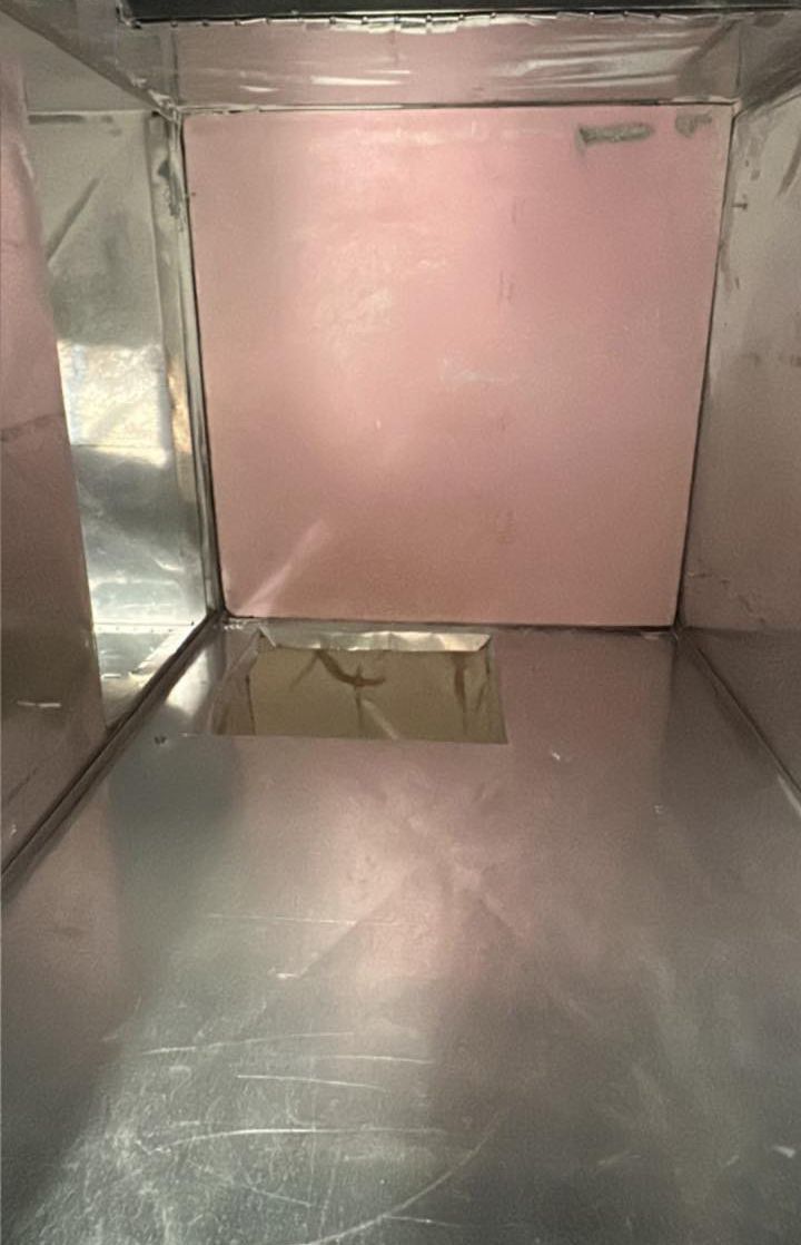 A stainless steel box with a pink wall and a hole in the floor.