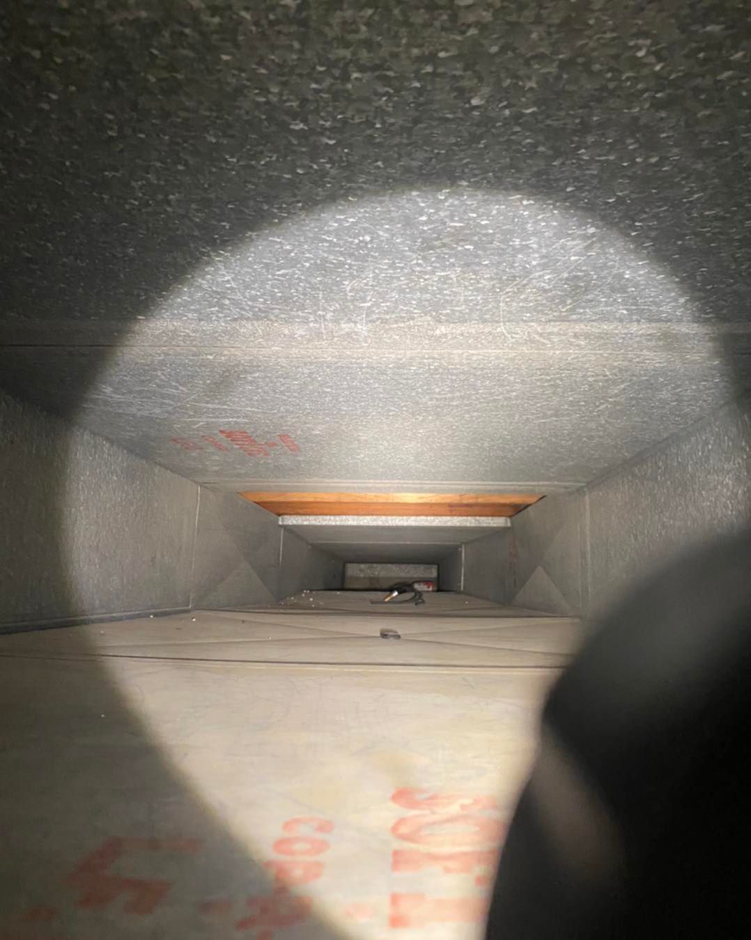 A person is looking down a duct with a flashlight.