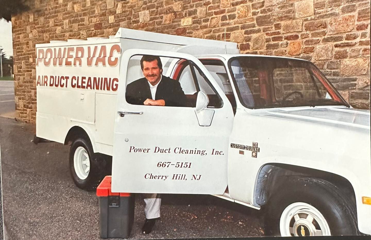 A man is sitting in the driver 's seat of a power vac air duct cleaning truck